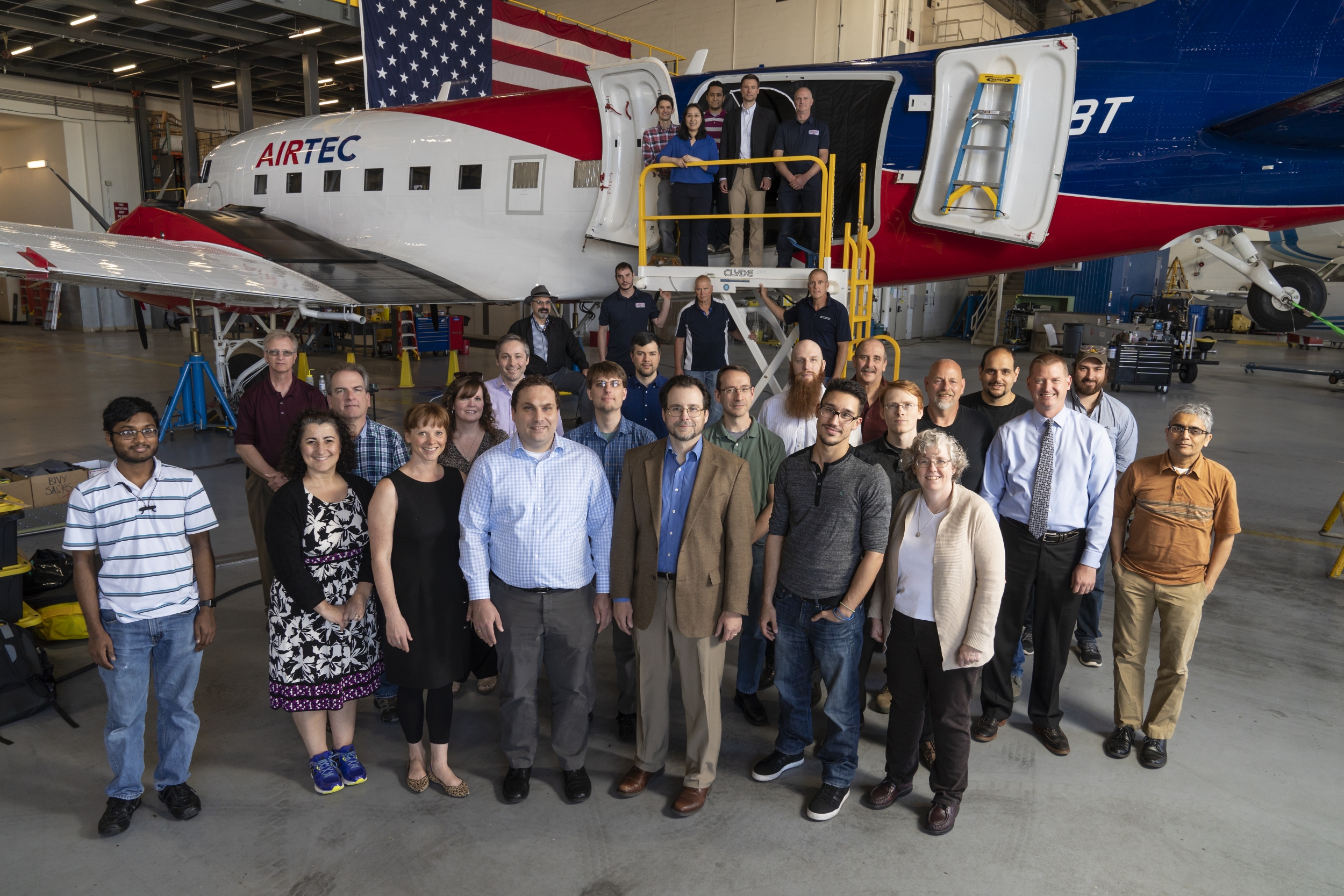 A group of about 30 people pose in front of an airplane