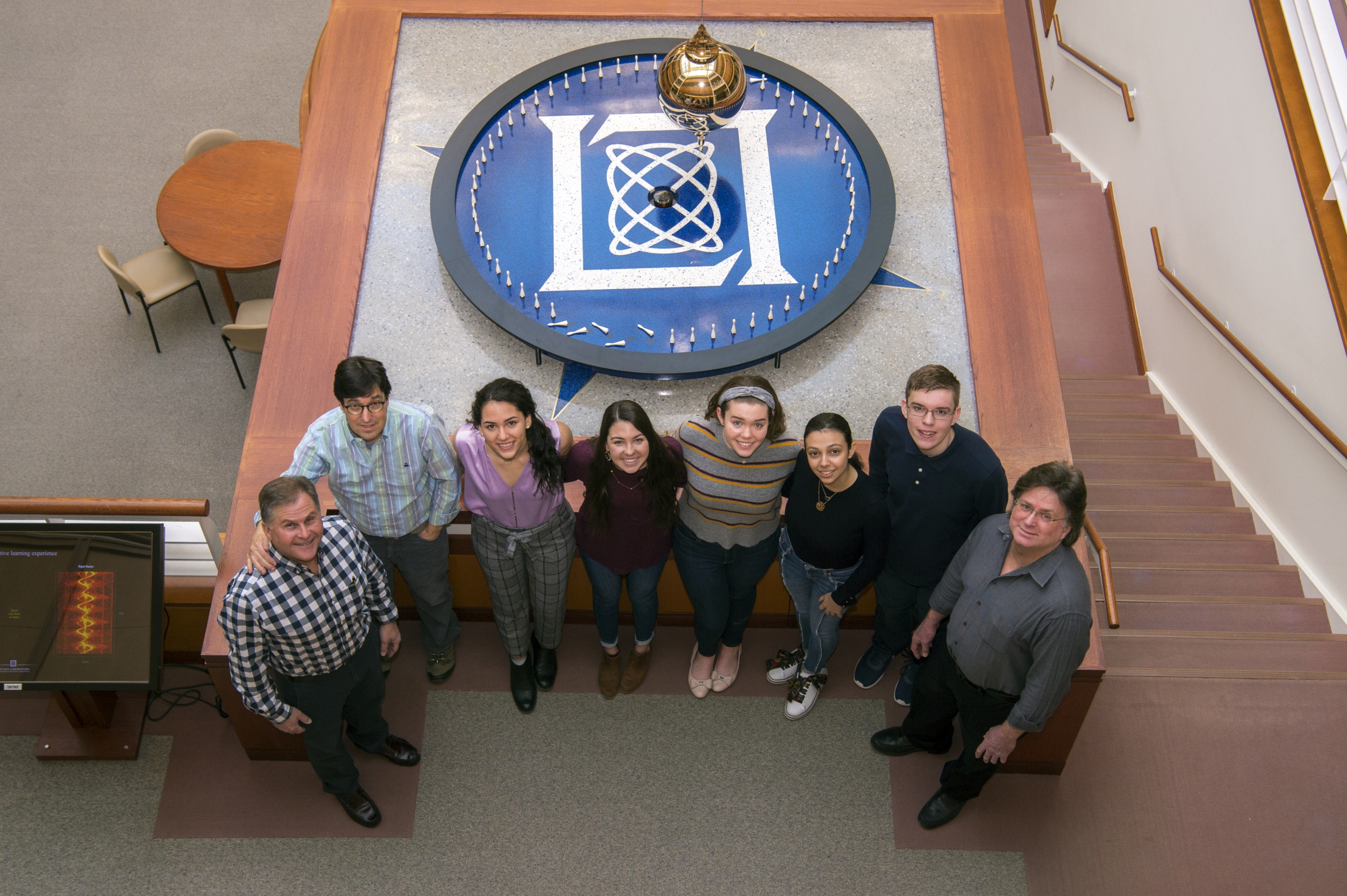 A group of students lab staff pose in front of a pendulum 
