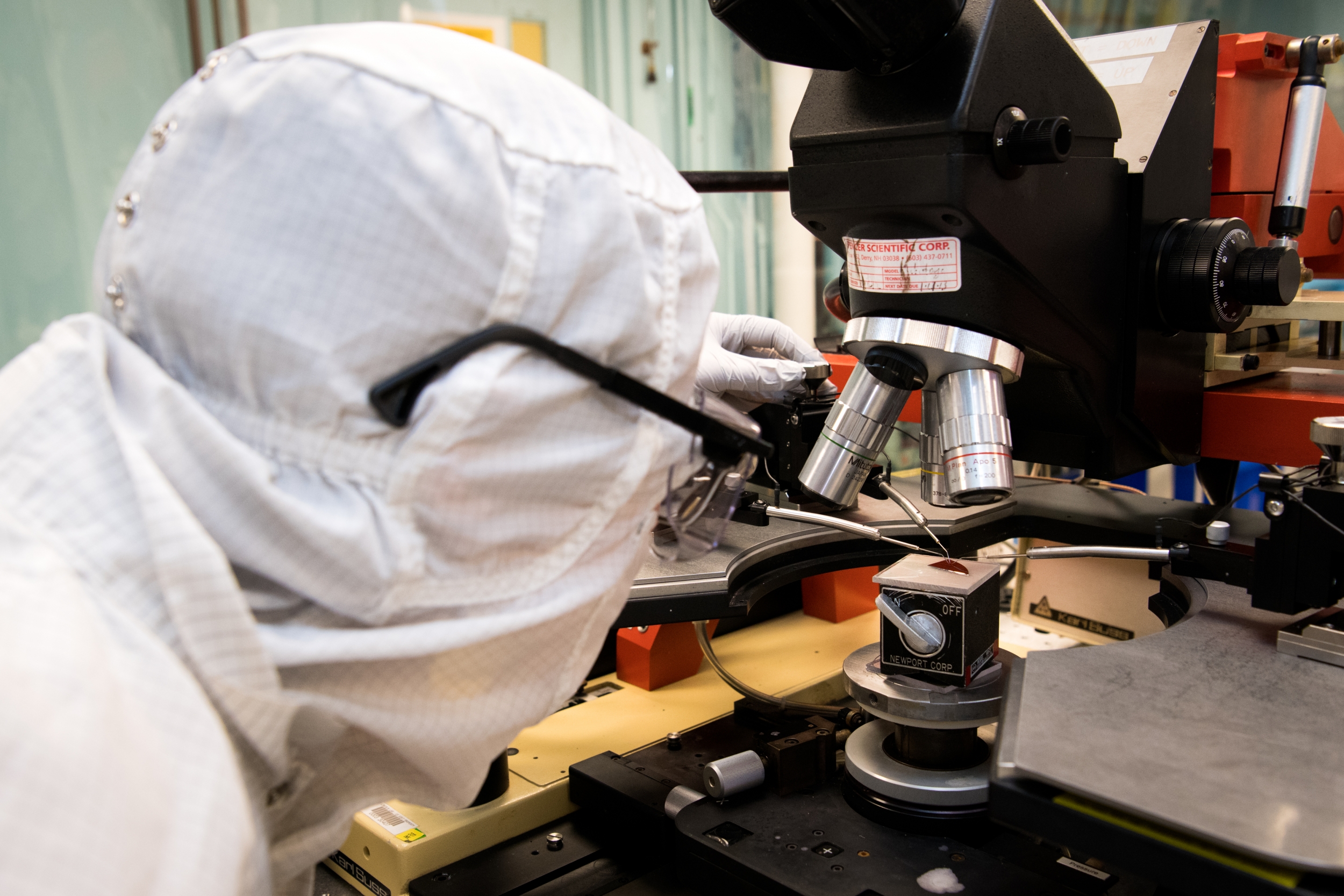 A researcher measures a battery performance while looking through a microscope.