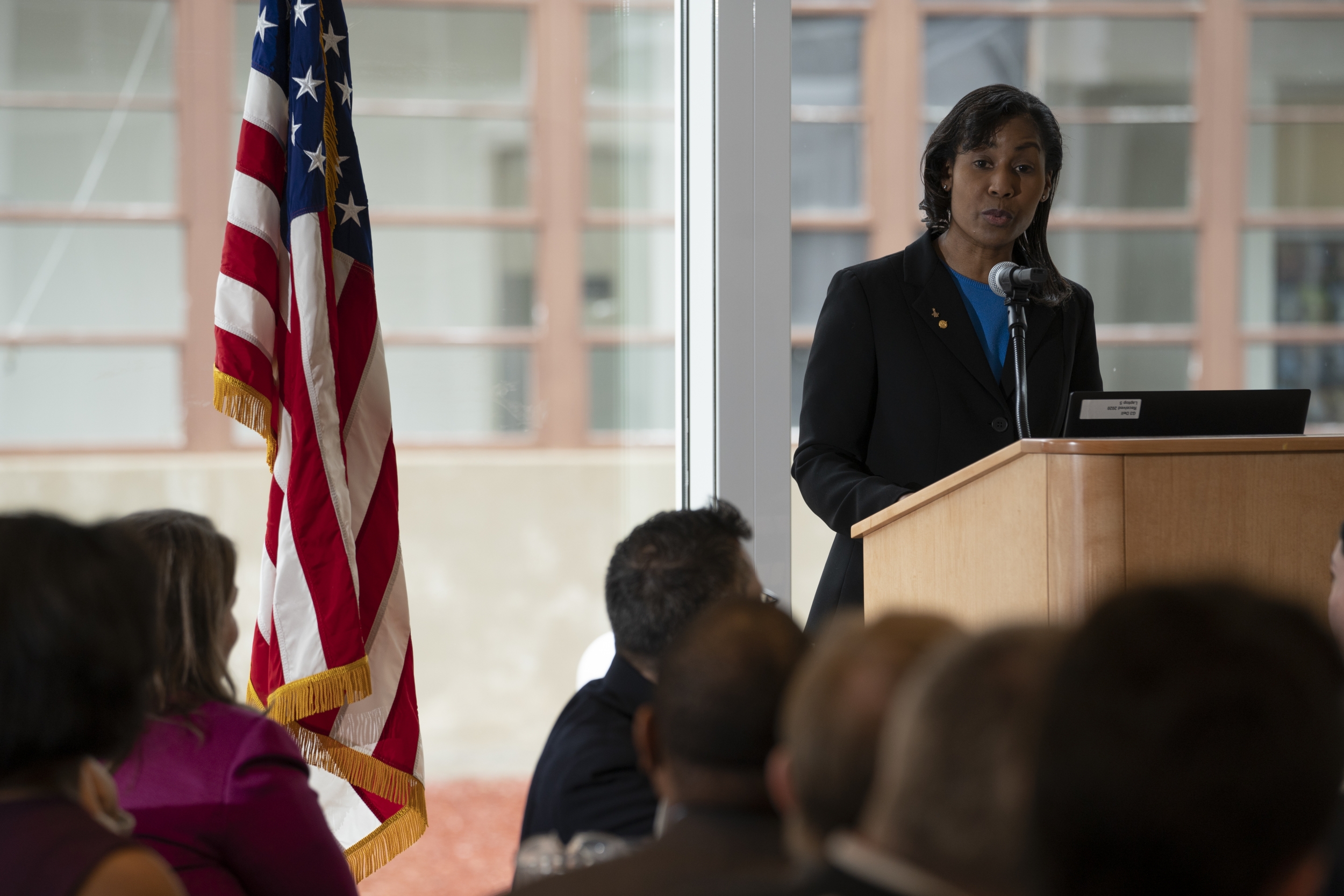 a photo of a woman standing and speaking at a podium next to an American flag