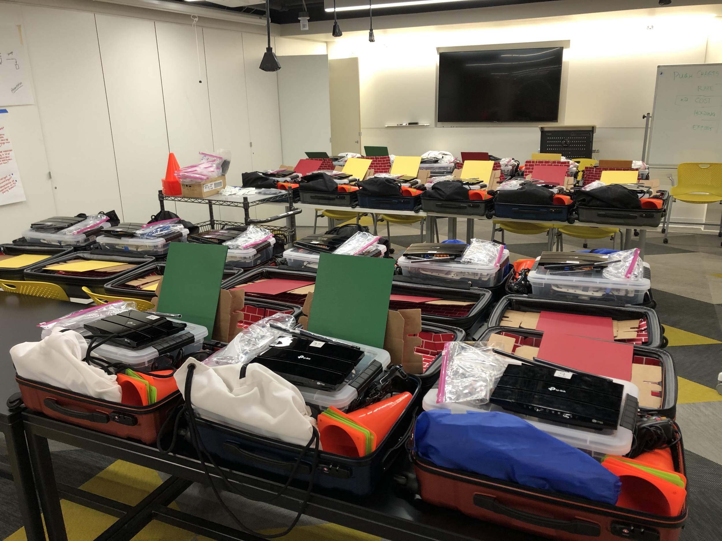 A photo showing about a dozen small robotic vehicles, each sitting inside a luggage suitcase. 