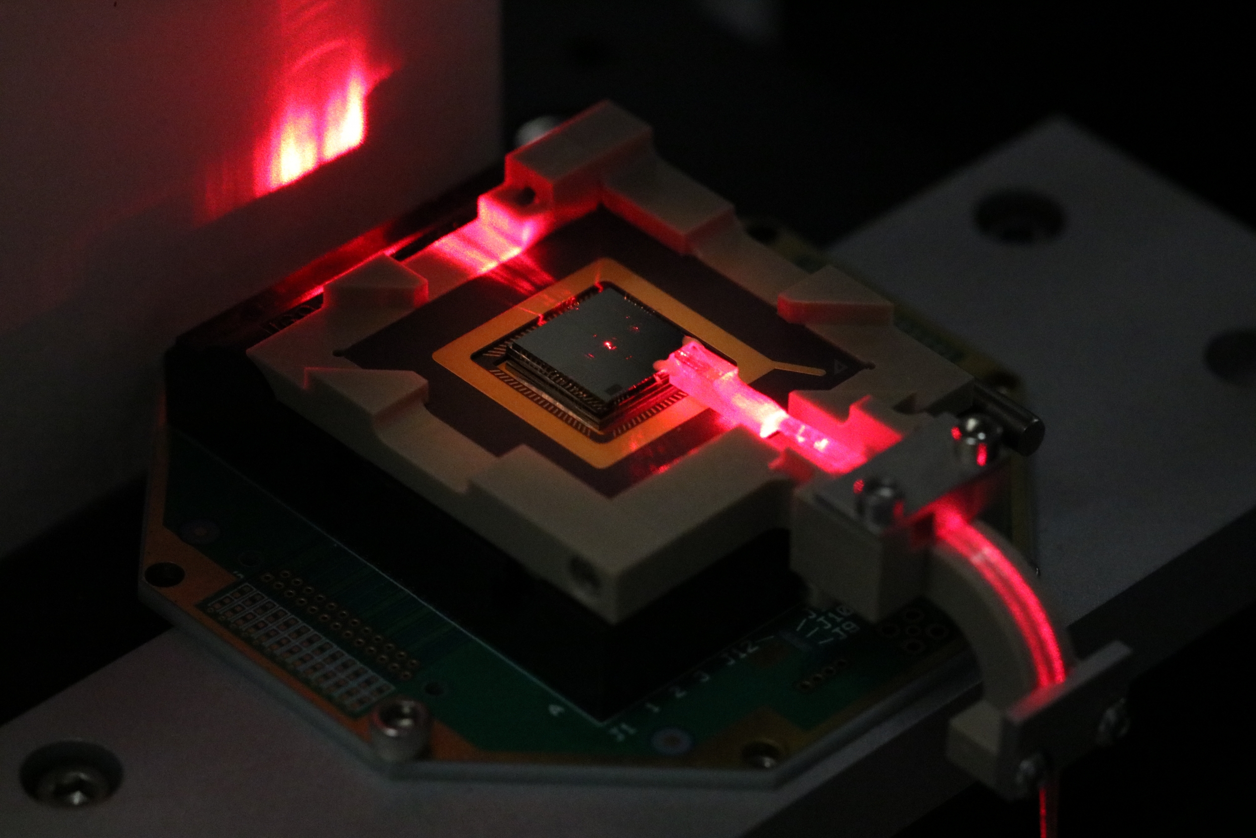 A square electronic chip with a red laser hitting the side of it