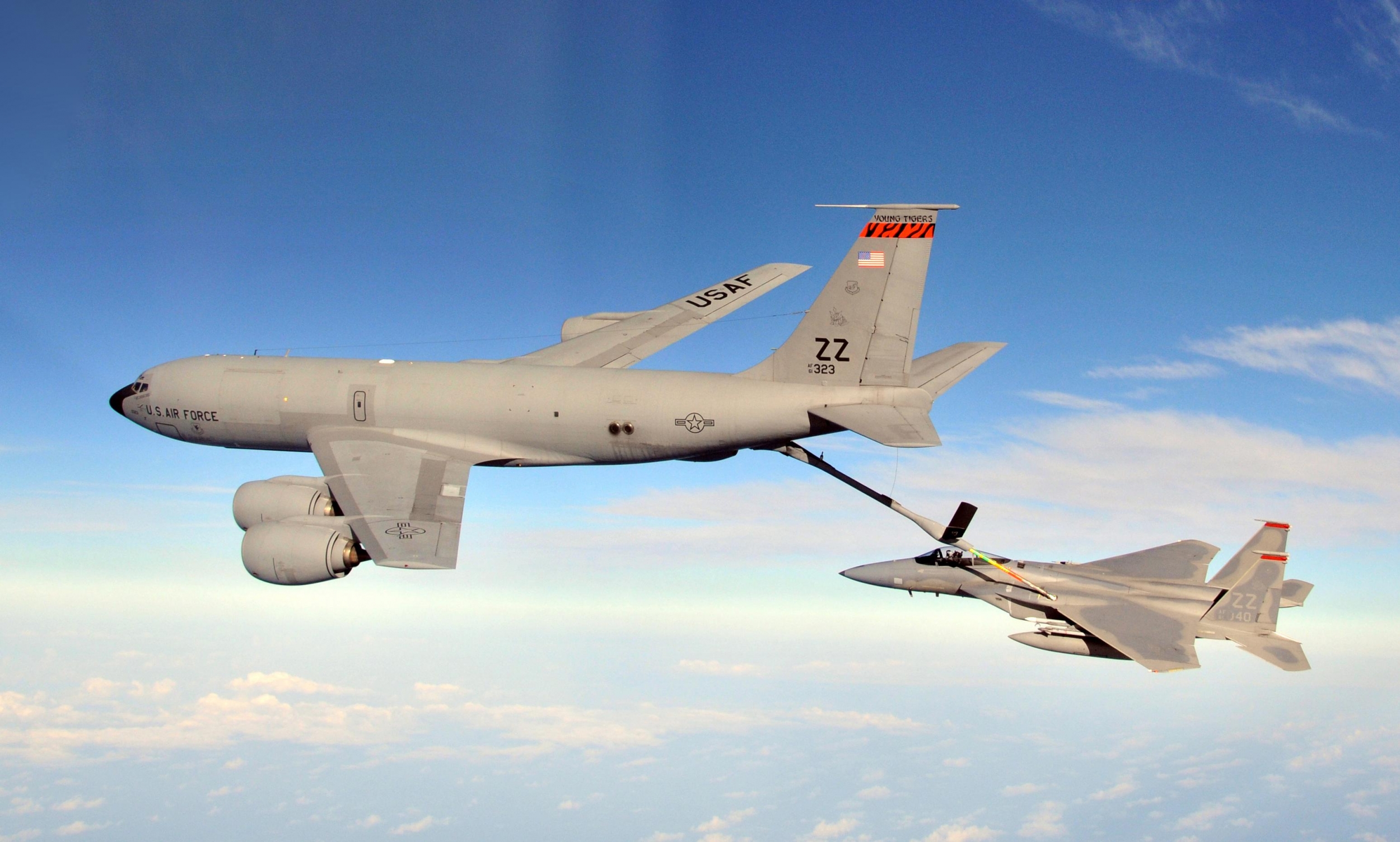 A large KC-135R tanker aircraft refuels an F-15 Eagle aircraft while they in mid air. 