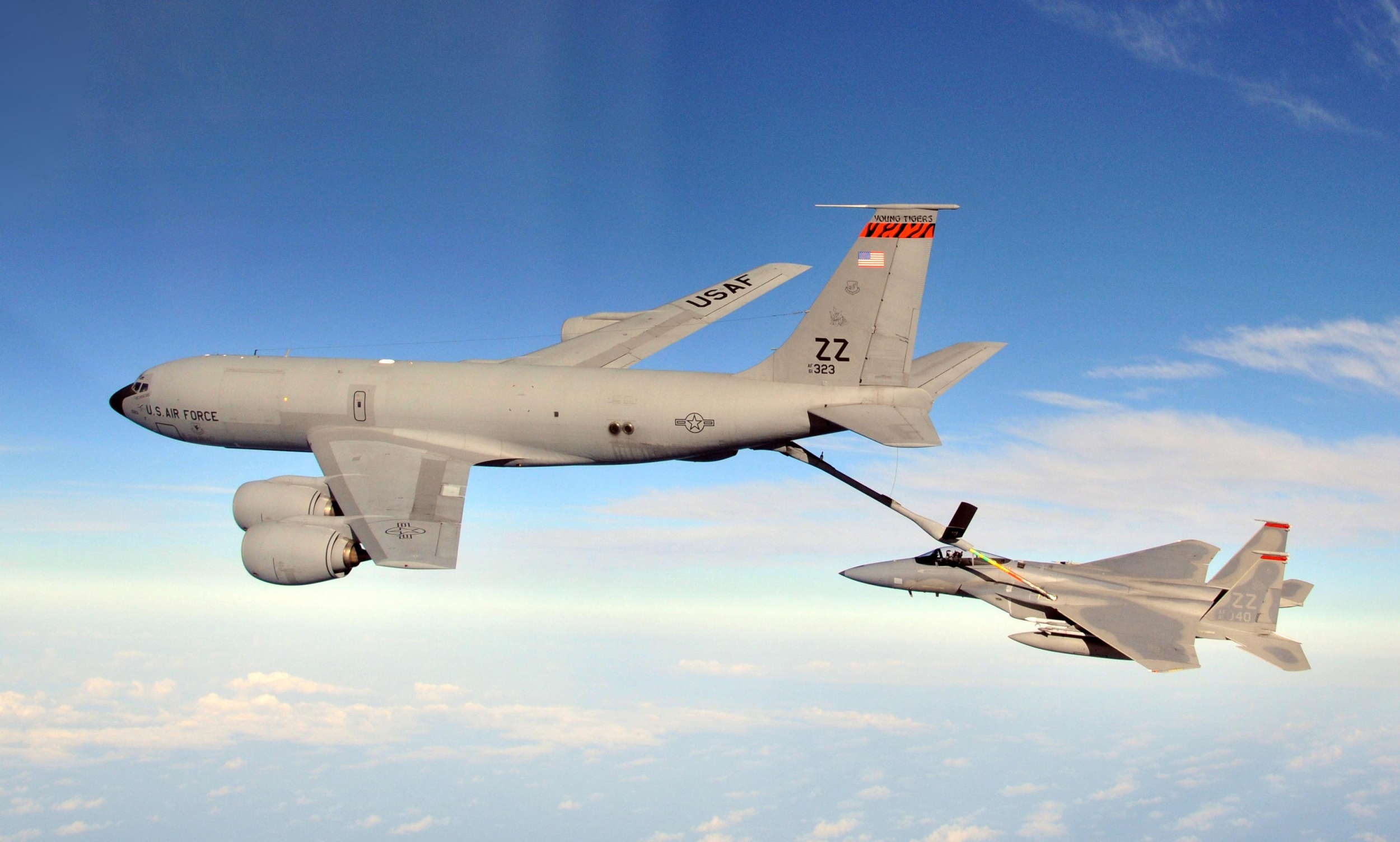 A large KC-135R tanker aircraft refuels an F-15 Eagle aircraft while they in mid air.