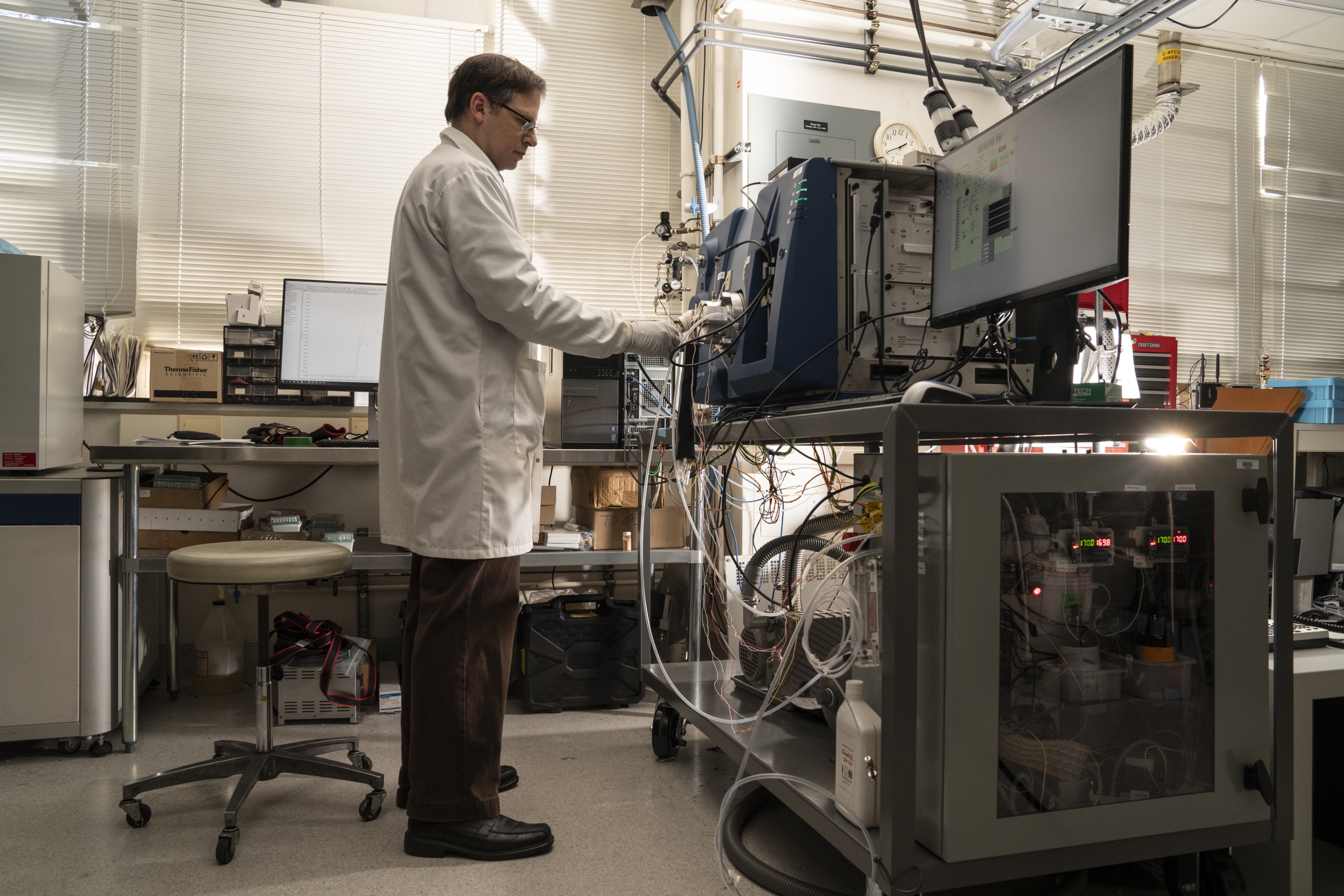 Laboratory staff member Ted Mendum stands while performing system checks on a mass spectrometer inside the laboratory. Photo: Glen Cooper