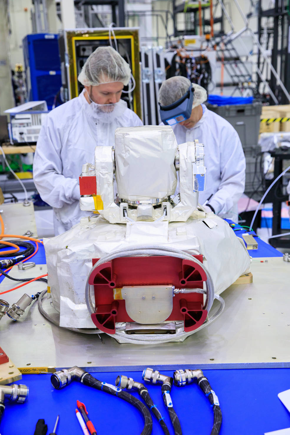 Two people inspect an optical communications payload in a cleanroom. 