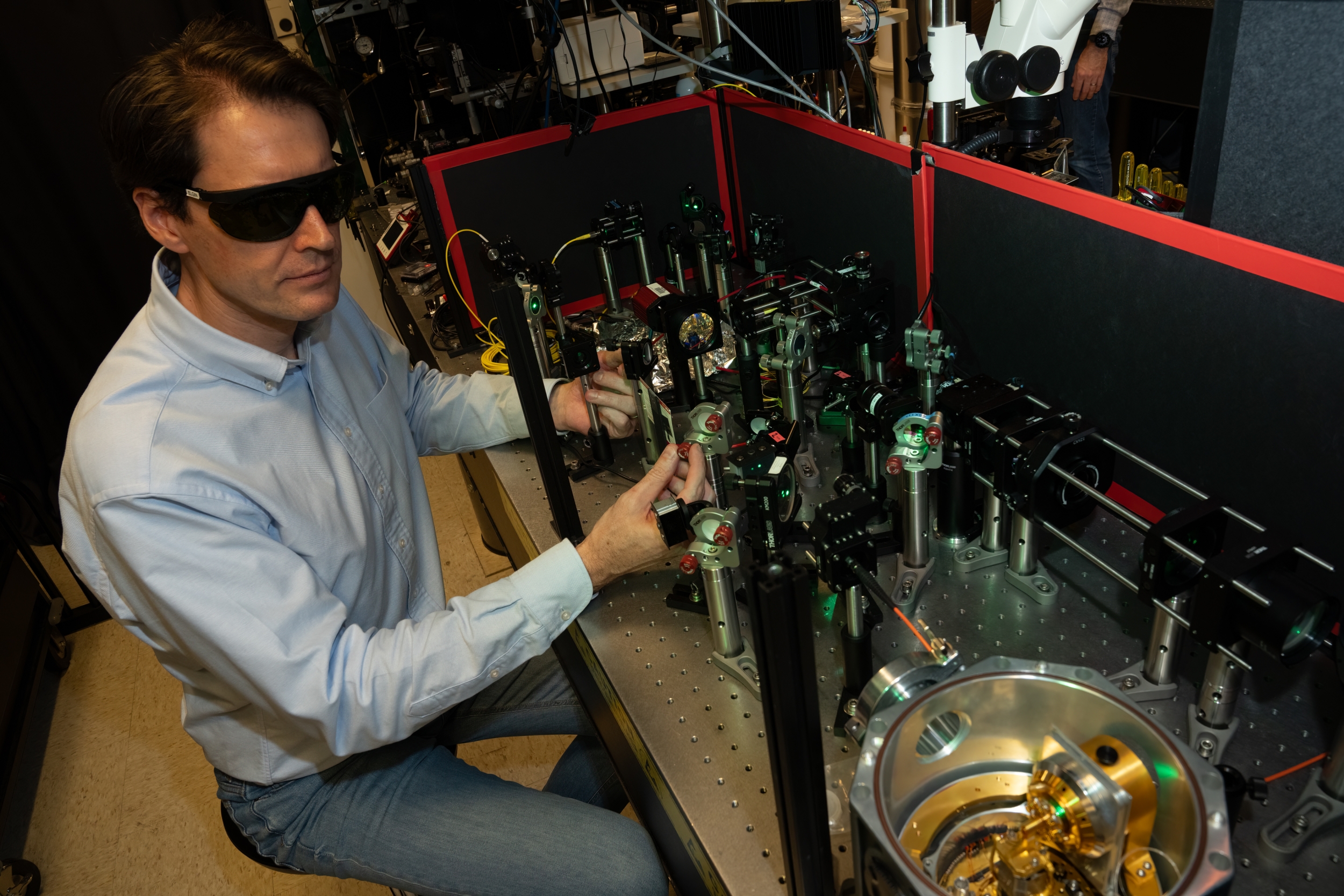 A staff member testes a green-glowing diamond in a cryogenic microscope.