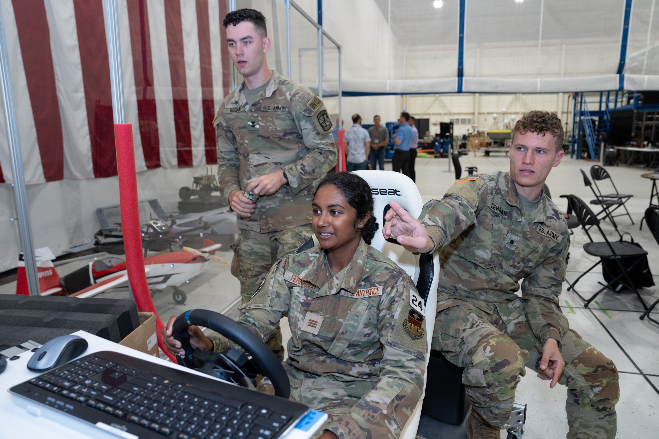 Three cadets are photographed; one is operating a steering wheel, controlling a robot off screen. The other two look on.