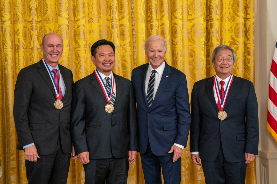 A photo of Eric Swanson, David Huang, and James Fujimoto with President Biden, smiling with medals around their necks. 