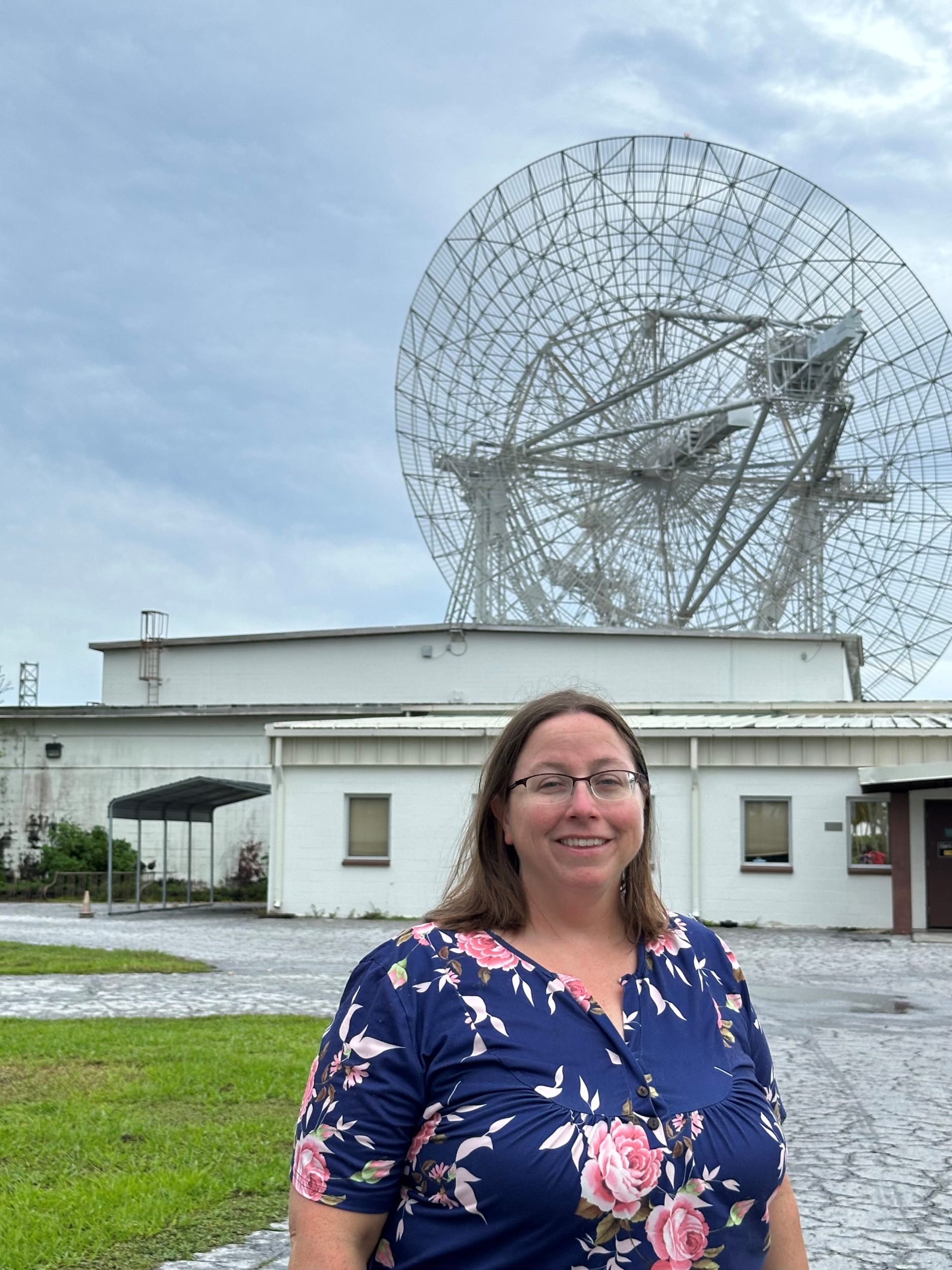 A woman stands in front of a large radar. 