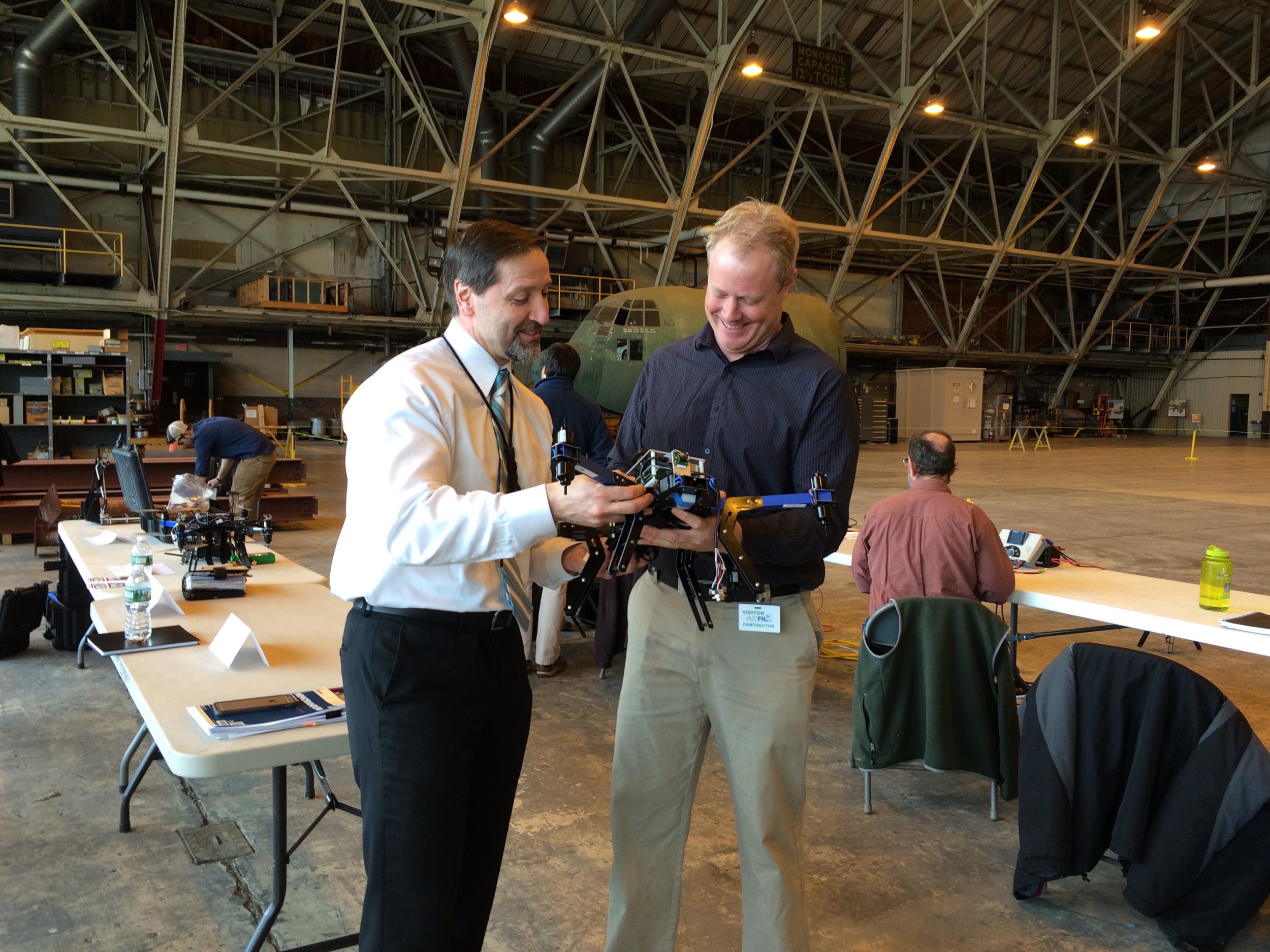 Two individuals hold and look at a drone at an Air Force Base indoor test range.