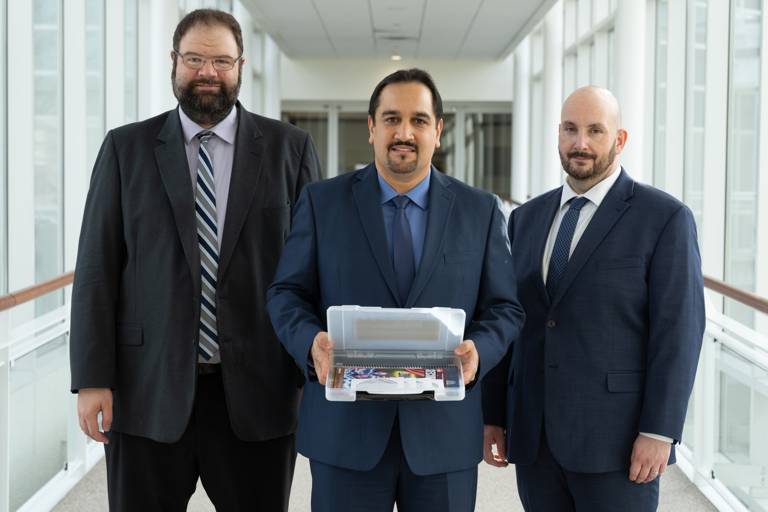 Three men stand side by side, with the person in the middle holding a box containing a software package.