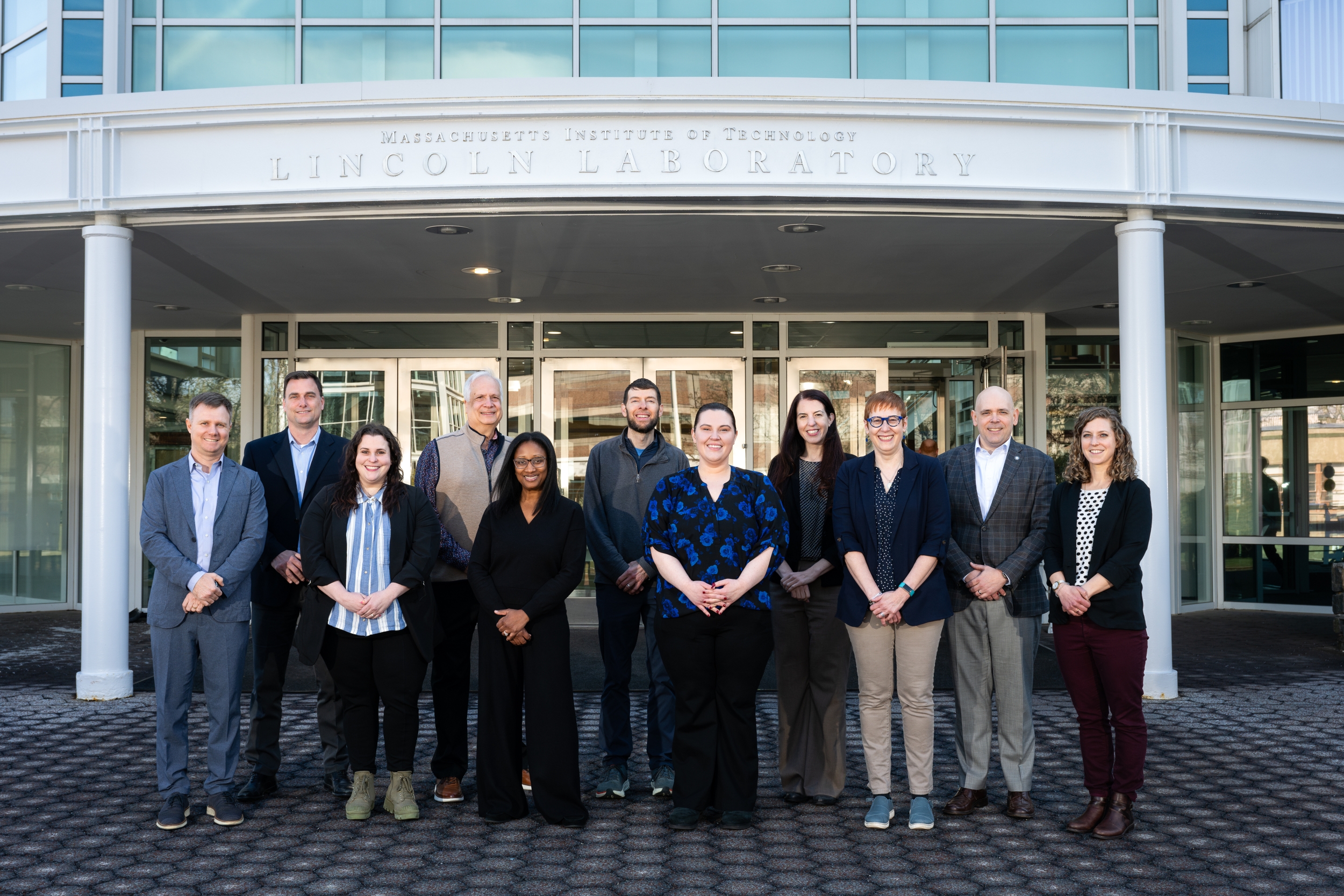 A group photo of PMI and MIT LL team outside of the main Lincoln Laboratory entrance.
