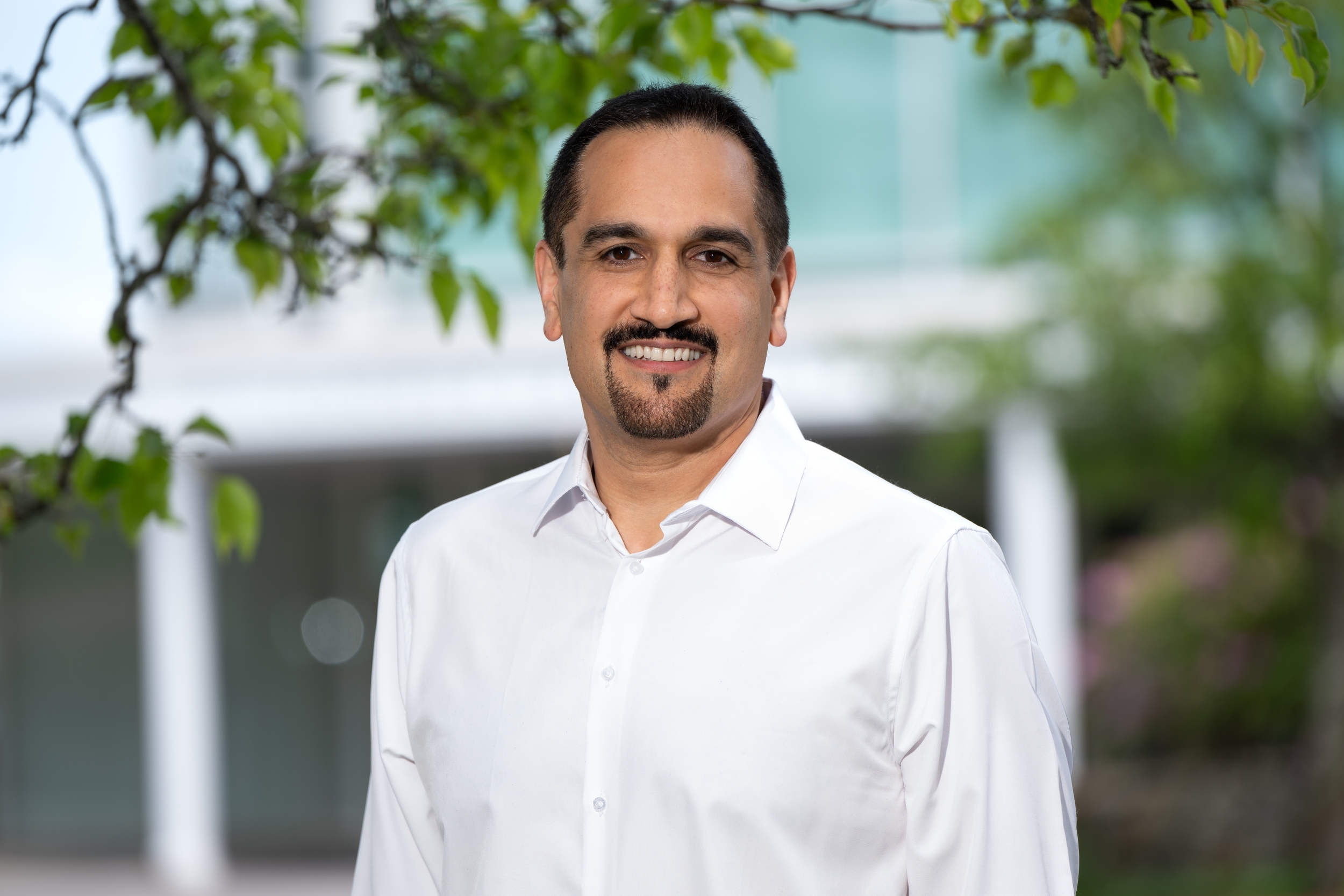 Hamed Okhravi smiles for a photo, standing outside with the front entrance displaying "Lincoln Laboratory" in the background.