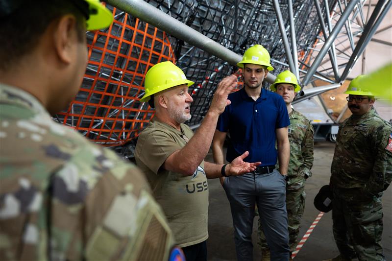 Jeffrey Dominick leads students on a tour of the Millstone Hill Radar. They wear yellow hardhats and listen attentively to Dominick's explanation as he gestures.