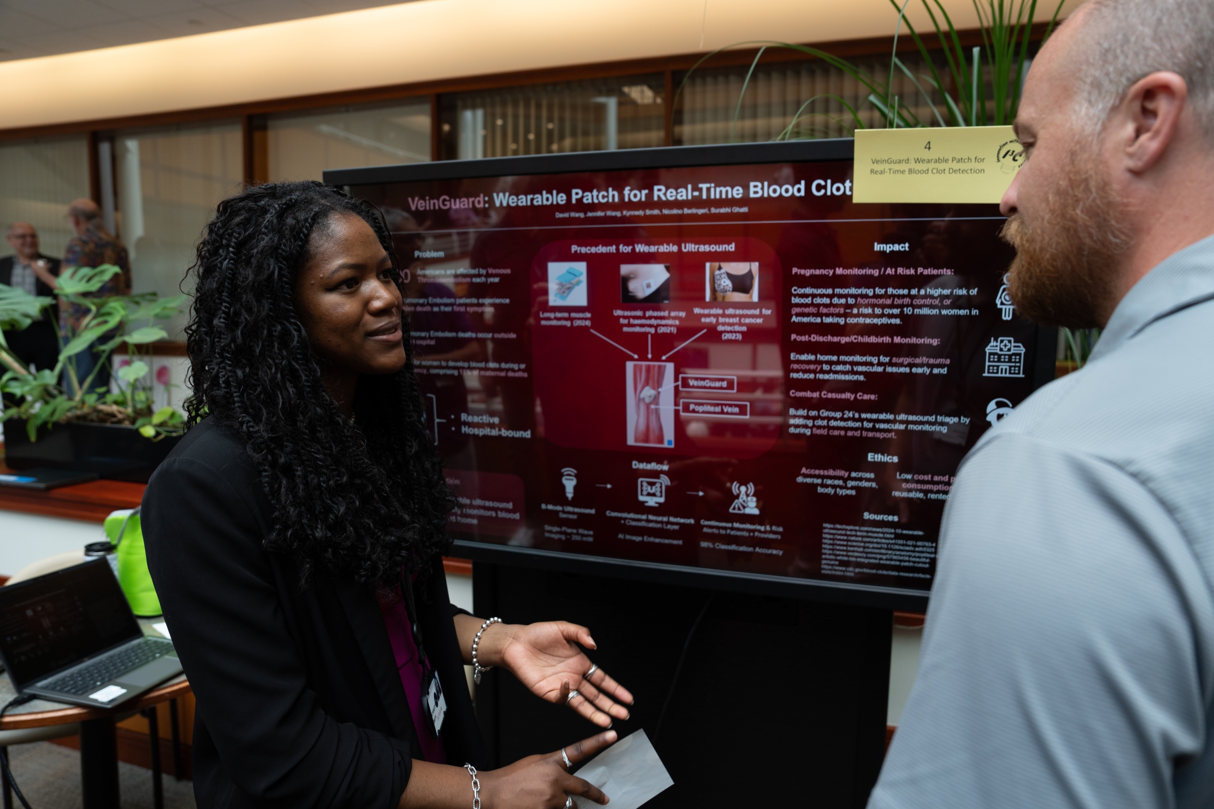  Intern Kynnedy Smith stand in front of her team's poster while explaining her project to a Laboratory staff member.