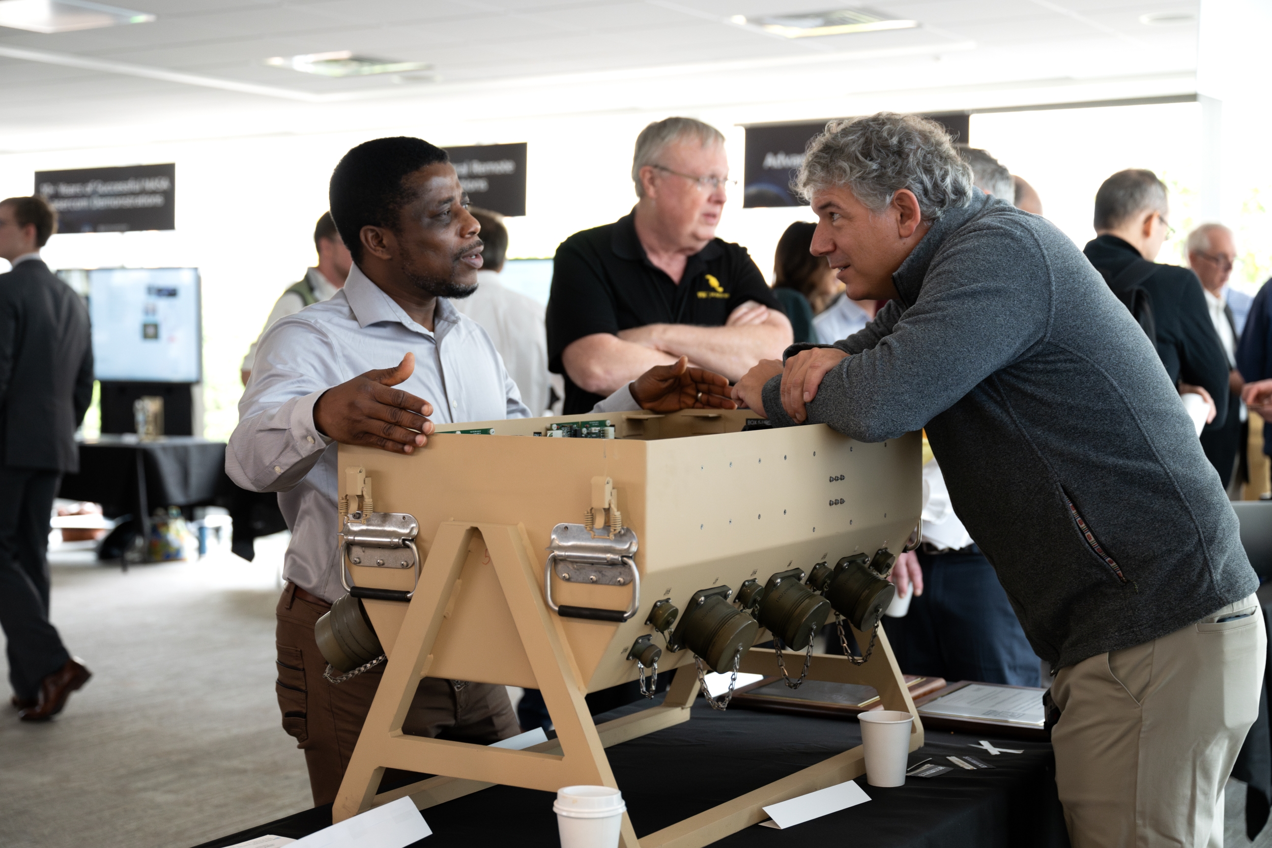 An expo attendee chats with a staff member about a technology that is a large pale brown box resting an an exhibition table.