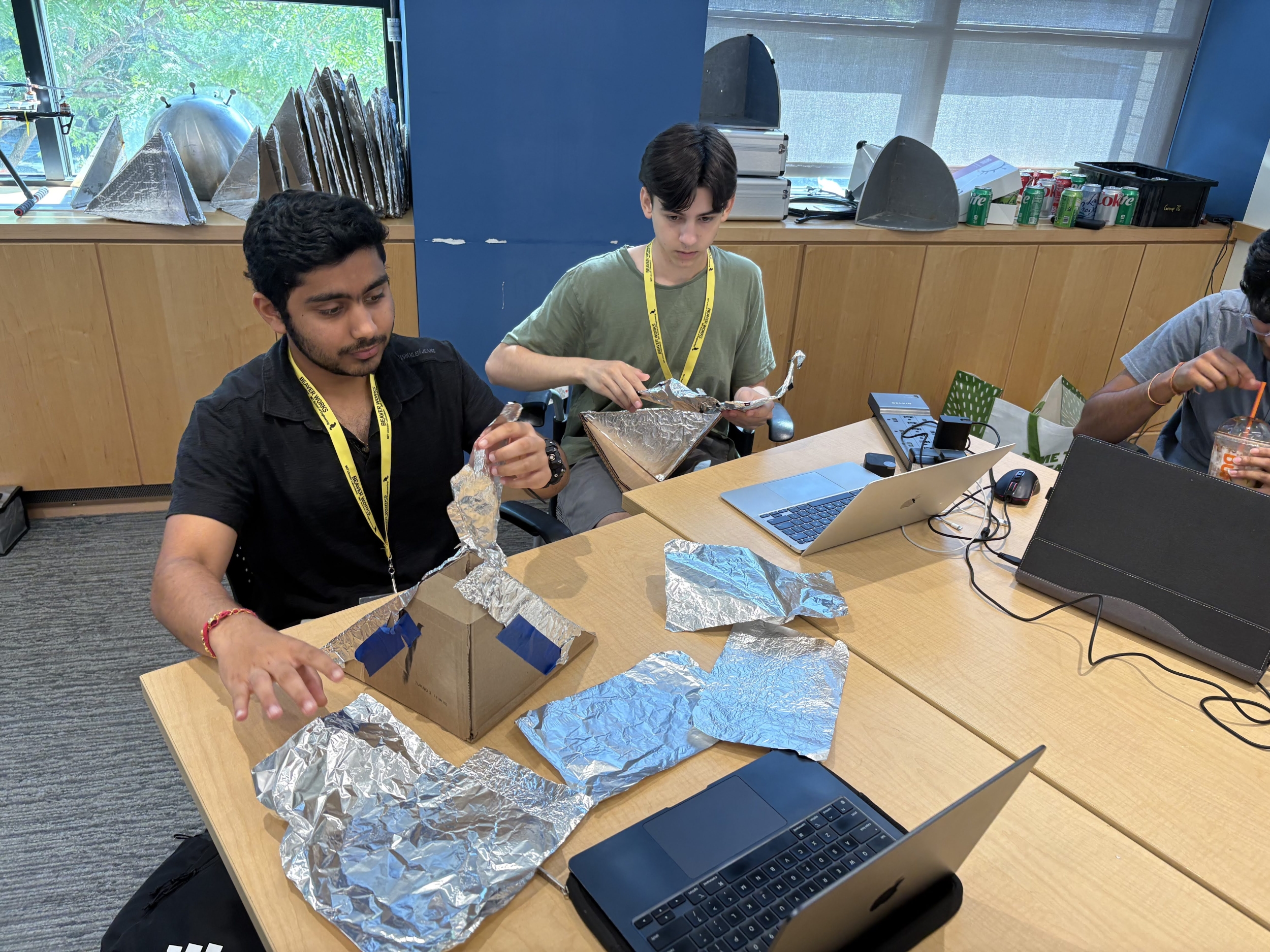 Two high school students tape foil squares onto self-built laptop-sized pyramid in order to make a radar reflector. 