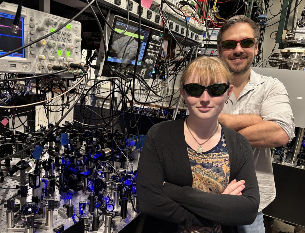 Lincoln Laboratory researchers Lucy Gray Shamel and Will Setzer wear protective glasses while standing next to the optics systems they used for the research. 