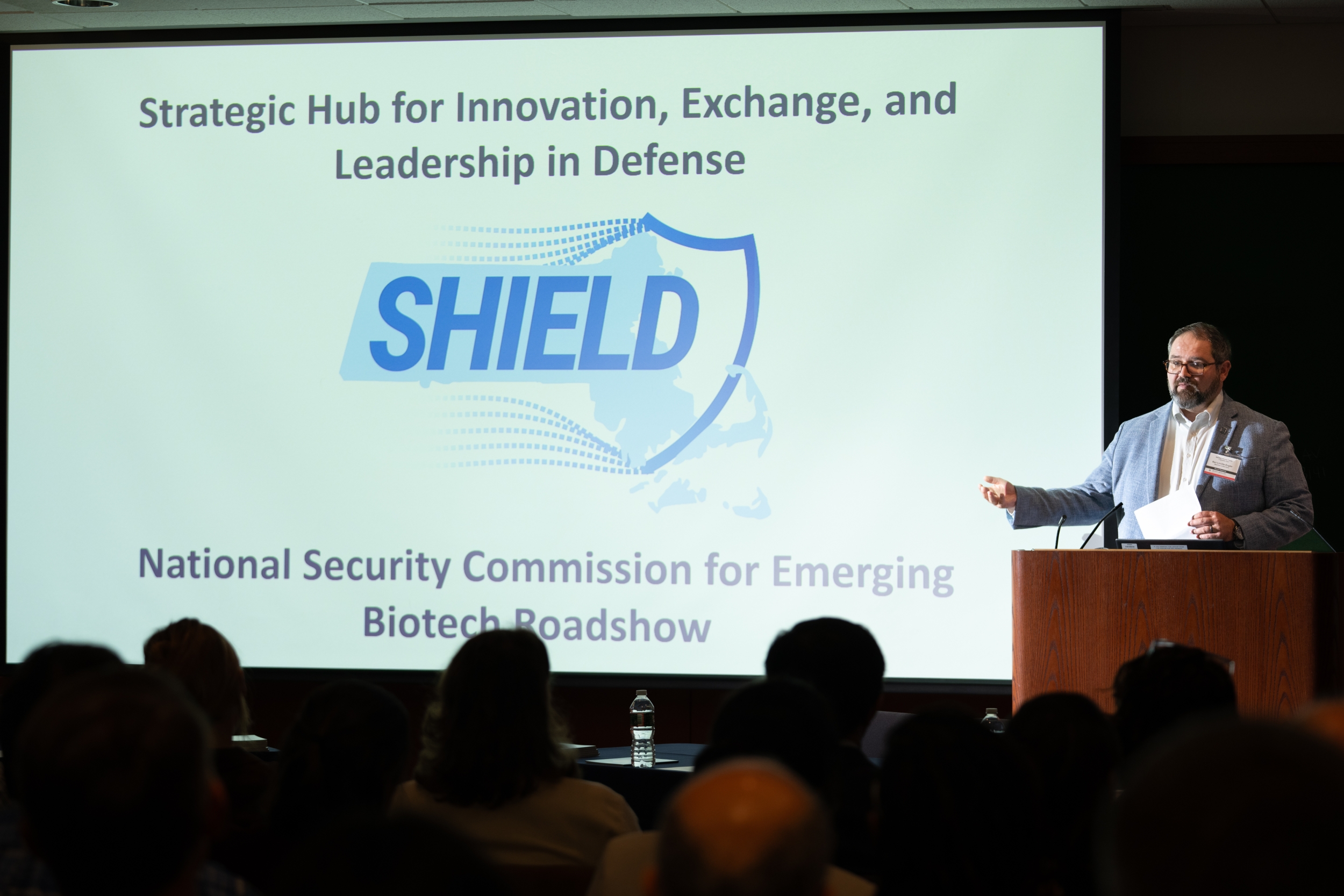 Ben Linville-Engler at a podium in front of a powerpoint slide that says "SHIELD"