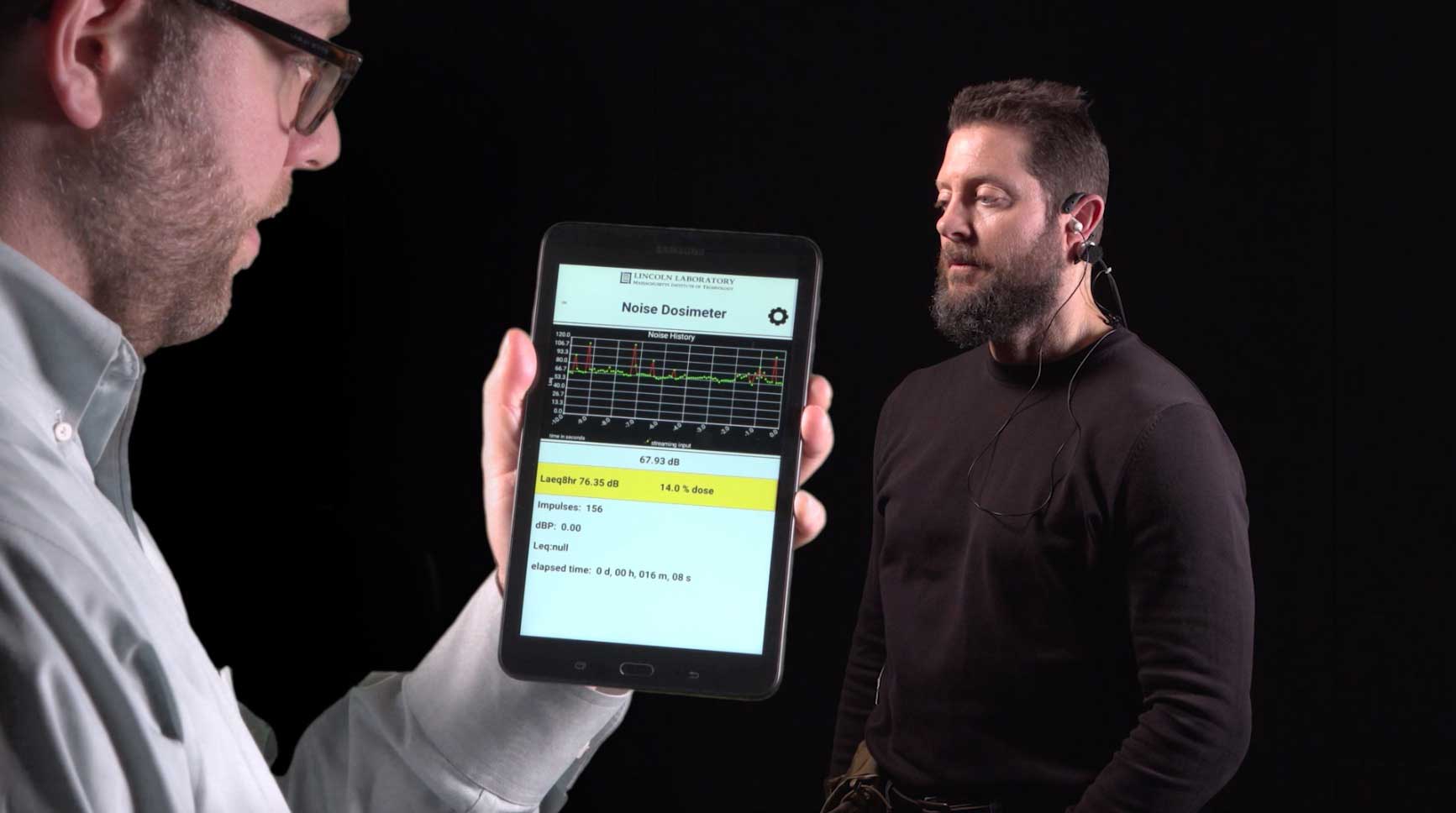 Photo of person wearing MNOISE microphones in ear and on body. User interface shows noise dosimeter levels.