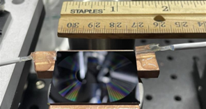 Photo of the spiral Mach-Zehnder interferometer on a 2.6 cm × 3.2 cm semiconductor chip shows the fiber arrays bonded to the input and output ports.