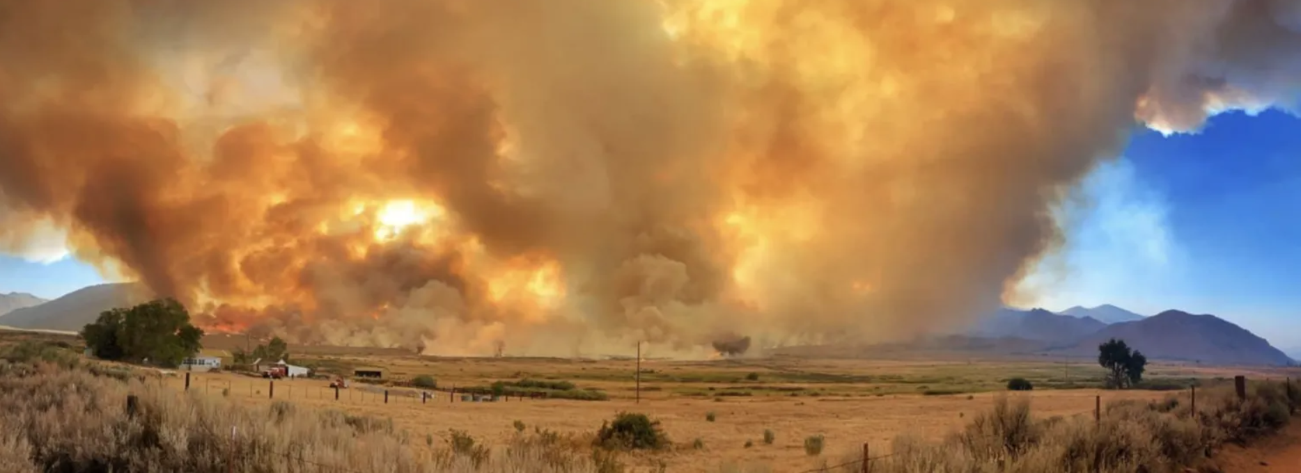 An image of the Slink wildfire showing flames and smoke rising over a field.