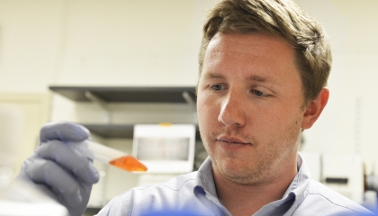 A staff member holds up a test tube filled with orange liquid