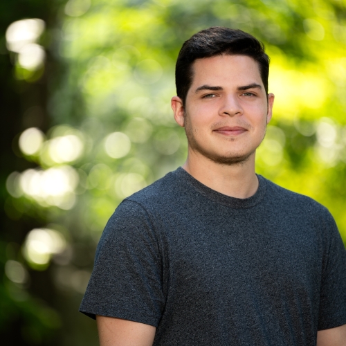 A portrait of David Langus Rodriguez outside with greenery in the background