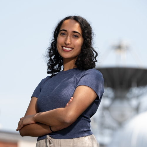 A portrait photograph of Sreshtaa Rajesh, with a radar antenna dish featured in the background.