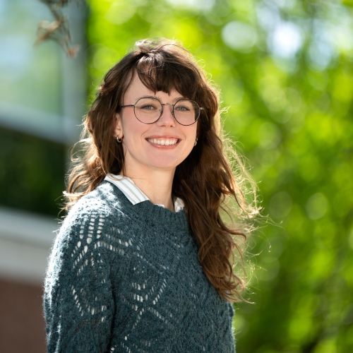 Photo of Emma McDaniel standing outside with a building and green trees in the background. 