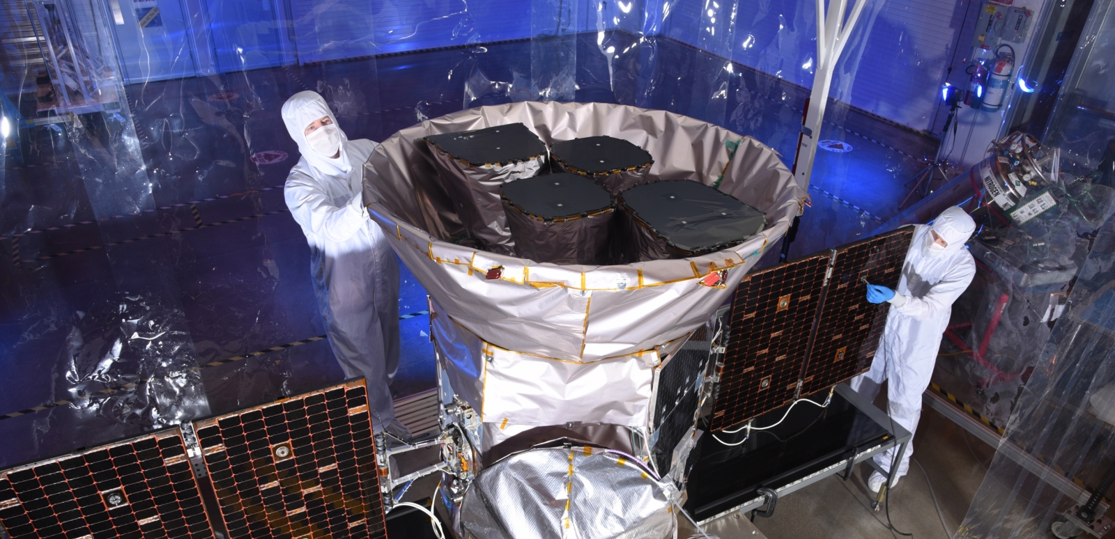 A photo of two scientists inspecting the tess satellite in a cleanroom environment.