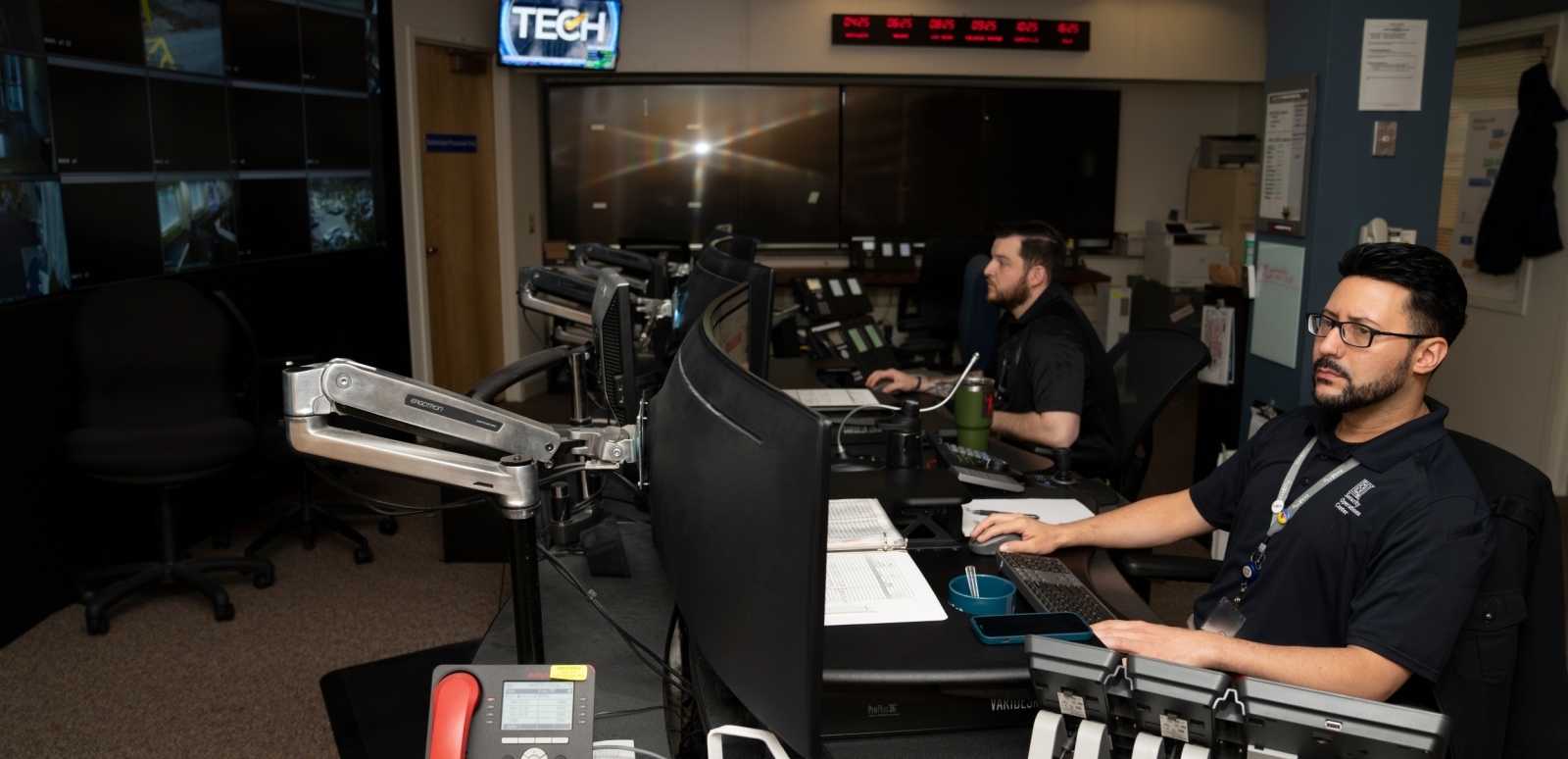Two Security Department employees work in front of several monitors.