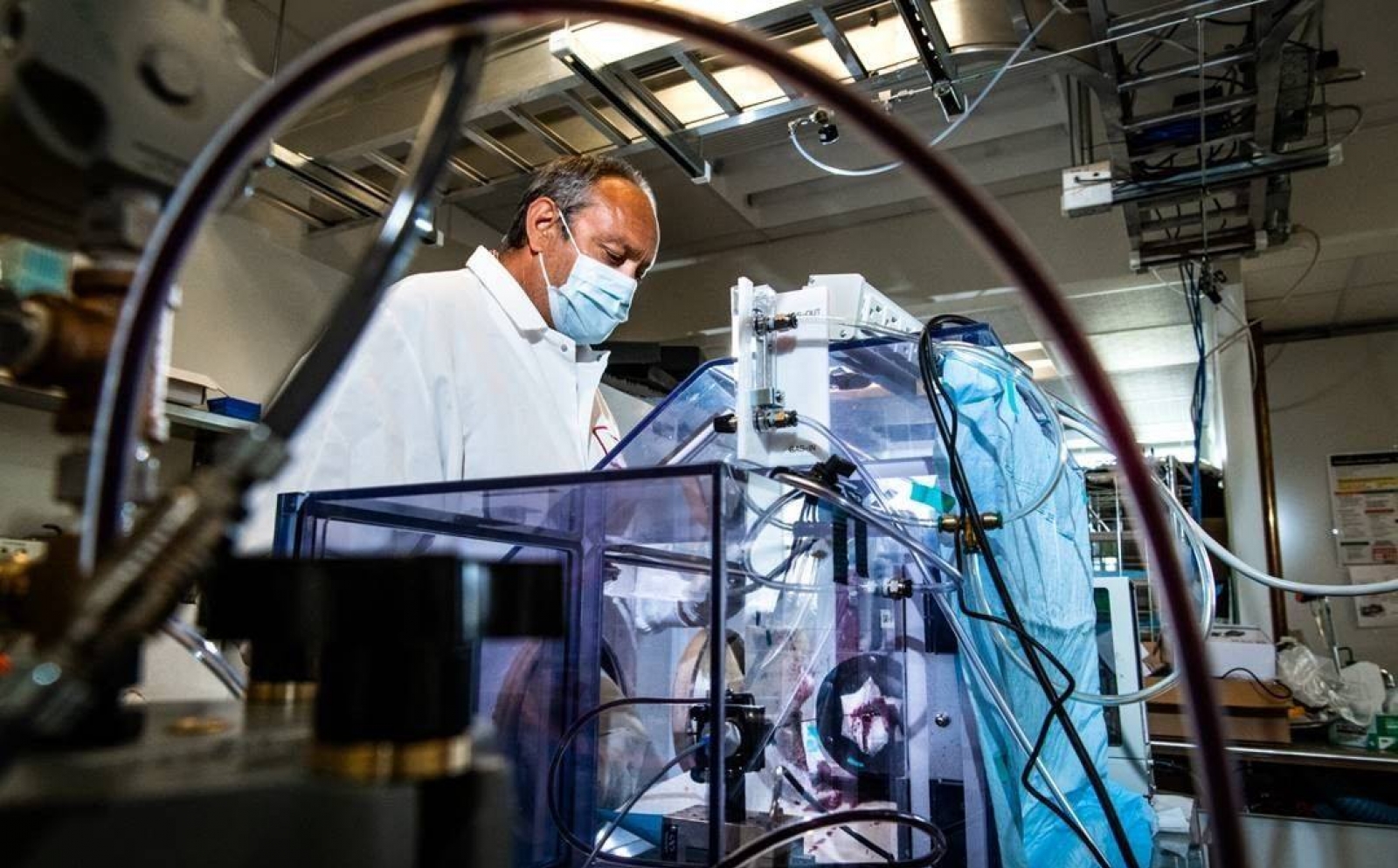 A man stands in a lab wearing a mask, in front of a big box setup where he is testing masks for air filtration. 