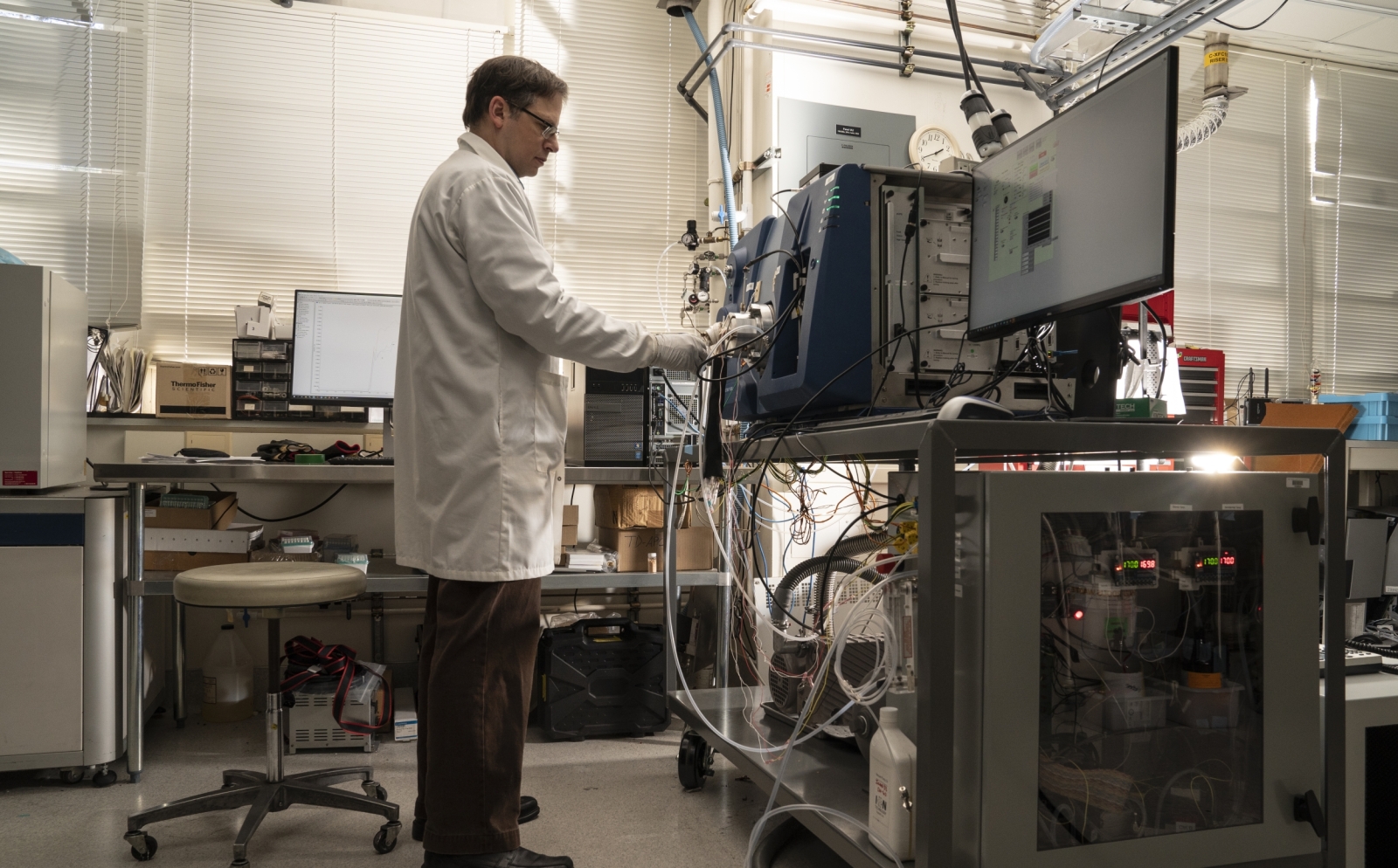 Laboratory staff member Ted Mendum stands while performing system checks on a mass spectrometer inside the laboratory. Photo: Glen Cooper