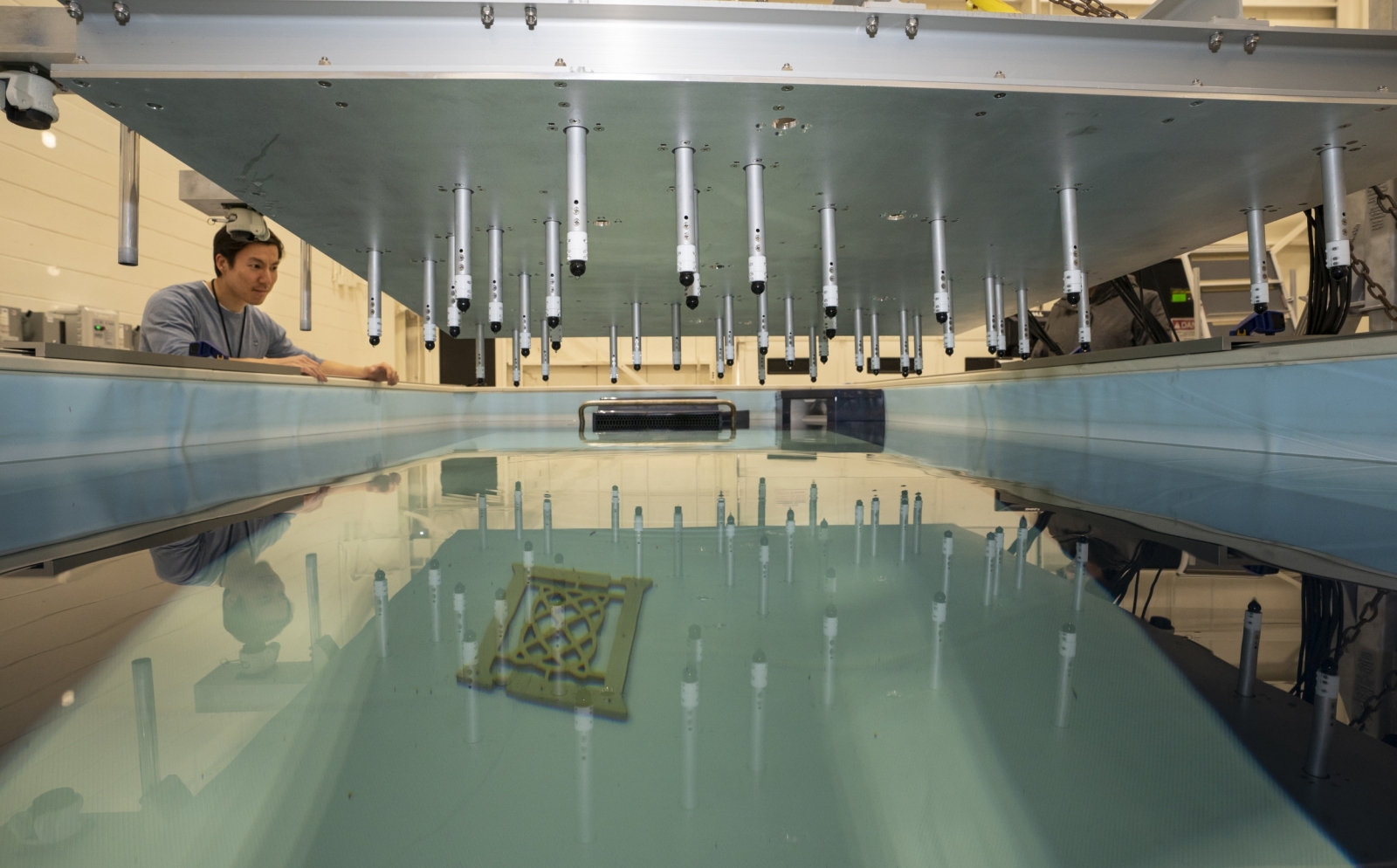 A person examines a sonar array suspended above a test tank. A Lincoln Laboratory logo is positioned near the bottom of the tank.