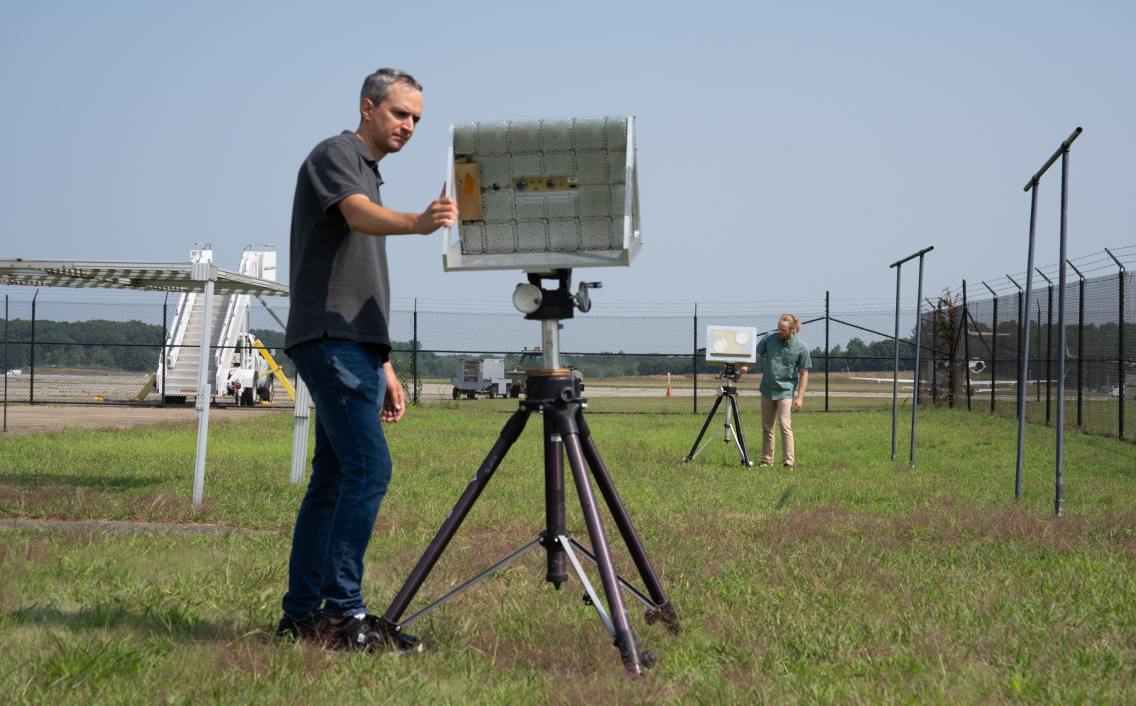 Two individuals inspect two radar and communications systems outdoors. 