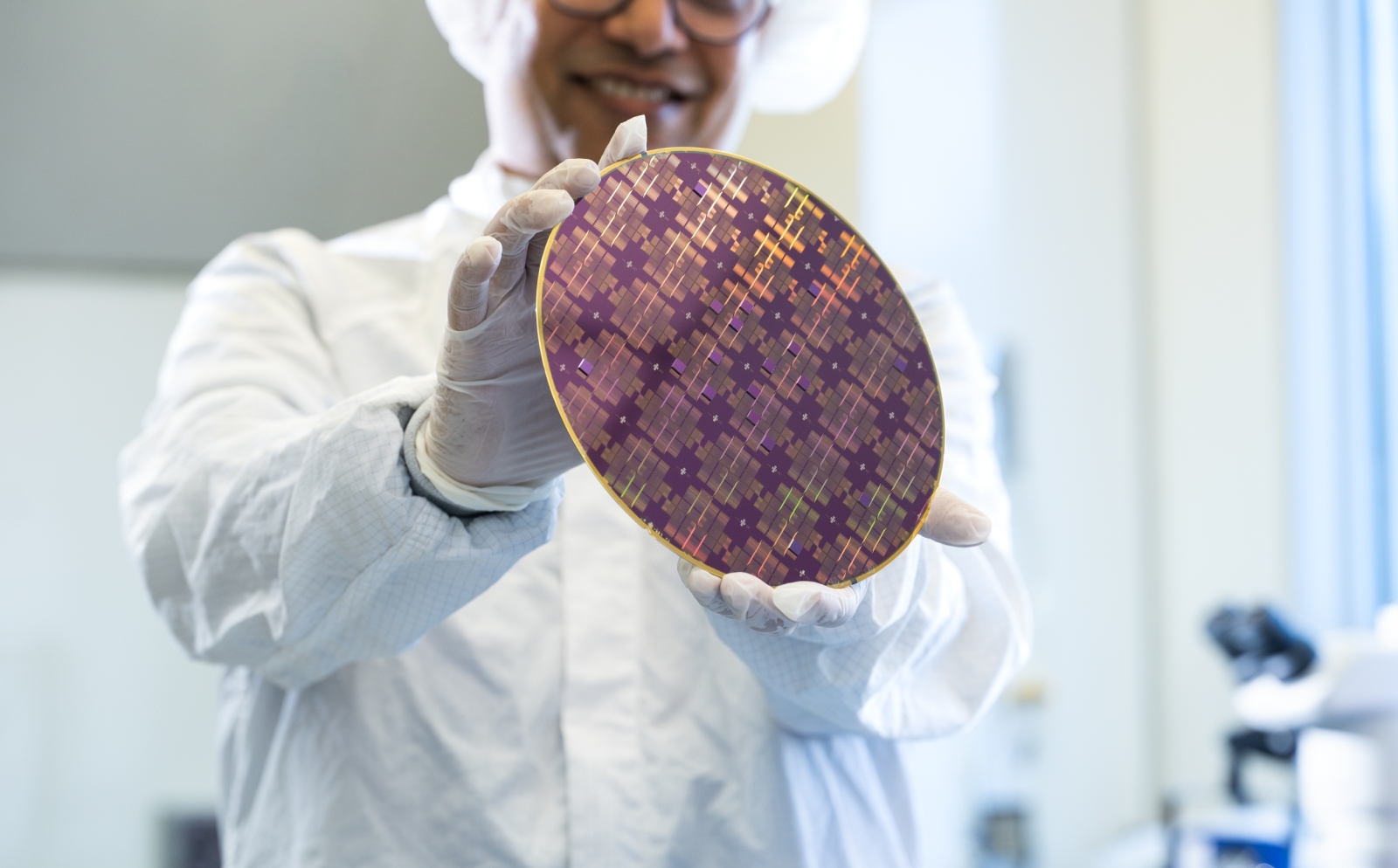 Rabindra Das (wearing microelectronics protective clothing within a fabrication space), holds an 8-inch wafer containing integrated circuits. 