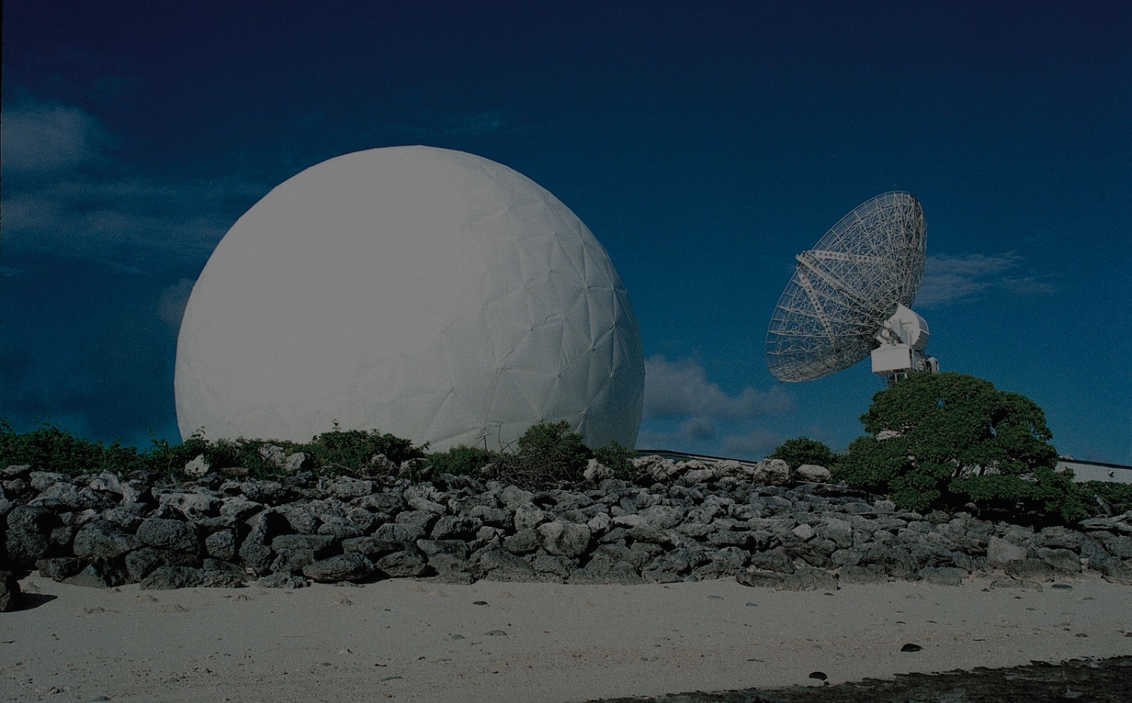A radar dome and radar dish sit next to a beach.