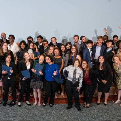 A group of about 25 people, mainly high school students, pose for a fun photo on an auditorium stage.