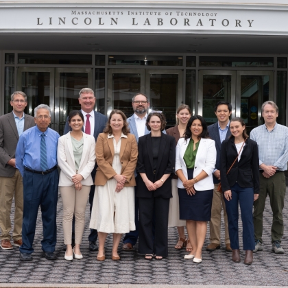 A group of 12 individuals standing in front of lincoln laboratory entrance. 