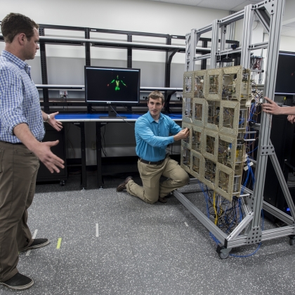 Researchers test the prototype standoff microwave imaging system. The antennas emit radio signals that reflect off the person standing in front of the array; the system processes the reflections to create the image on the monitors in the background.  