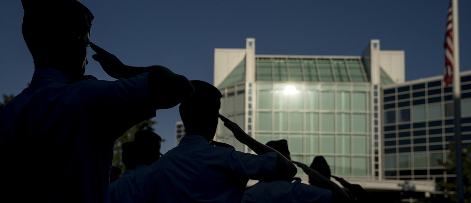 Members of the military salute in silhouette outside of MIT Lincoln Laboratory.
