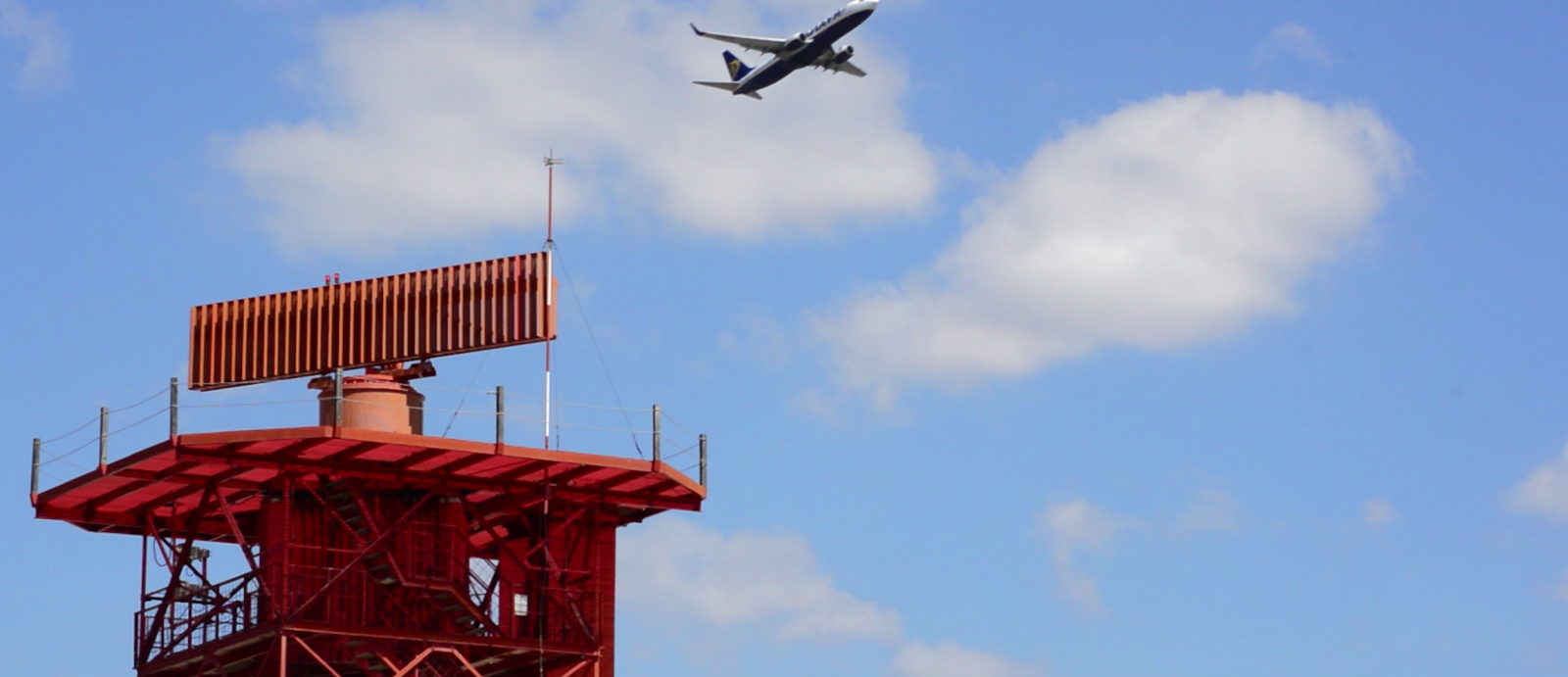 an orange antenna with an airplane in the sky behind it