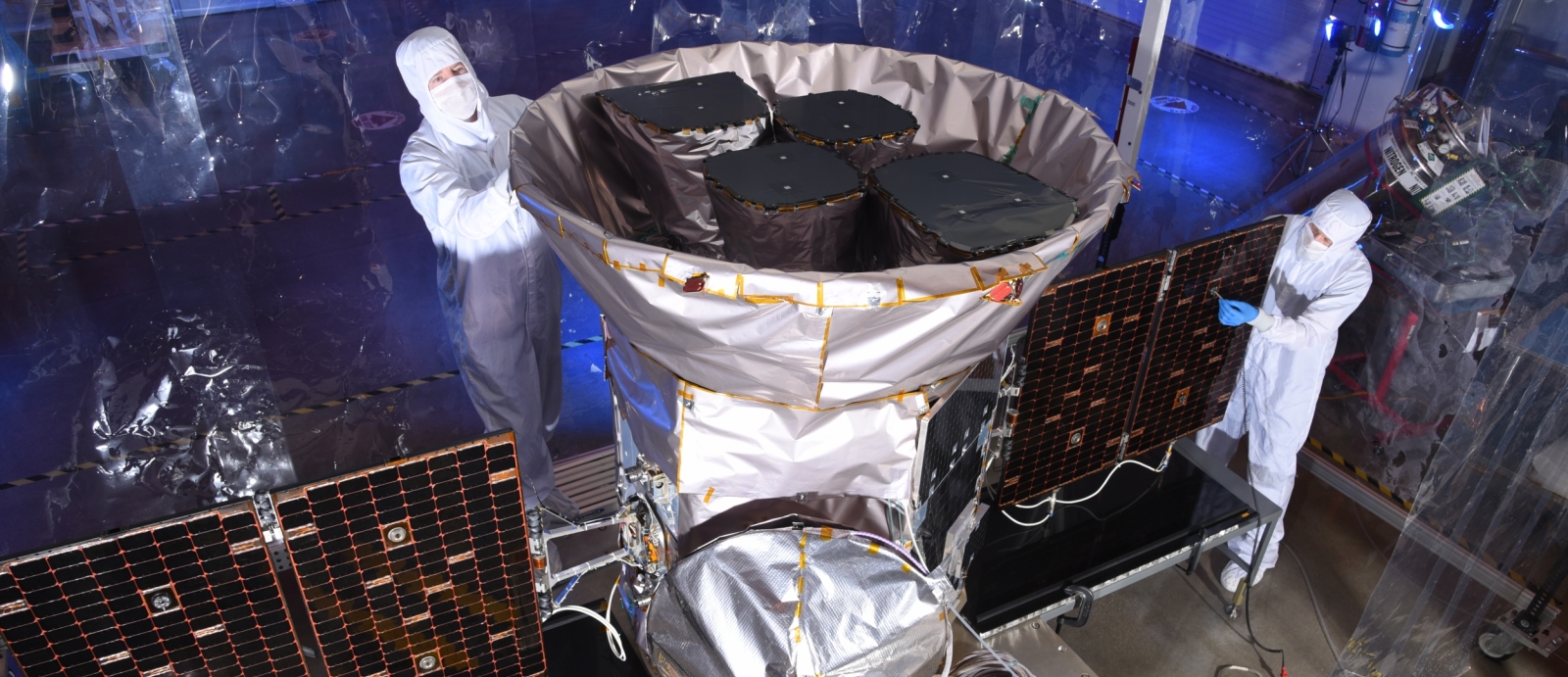 A photo of two scientists inspecting the tess satellite in a cleanroom environment.