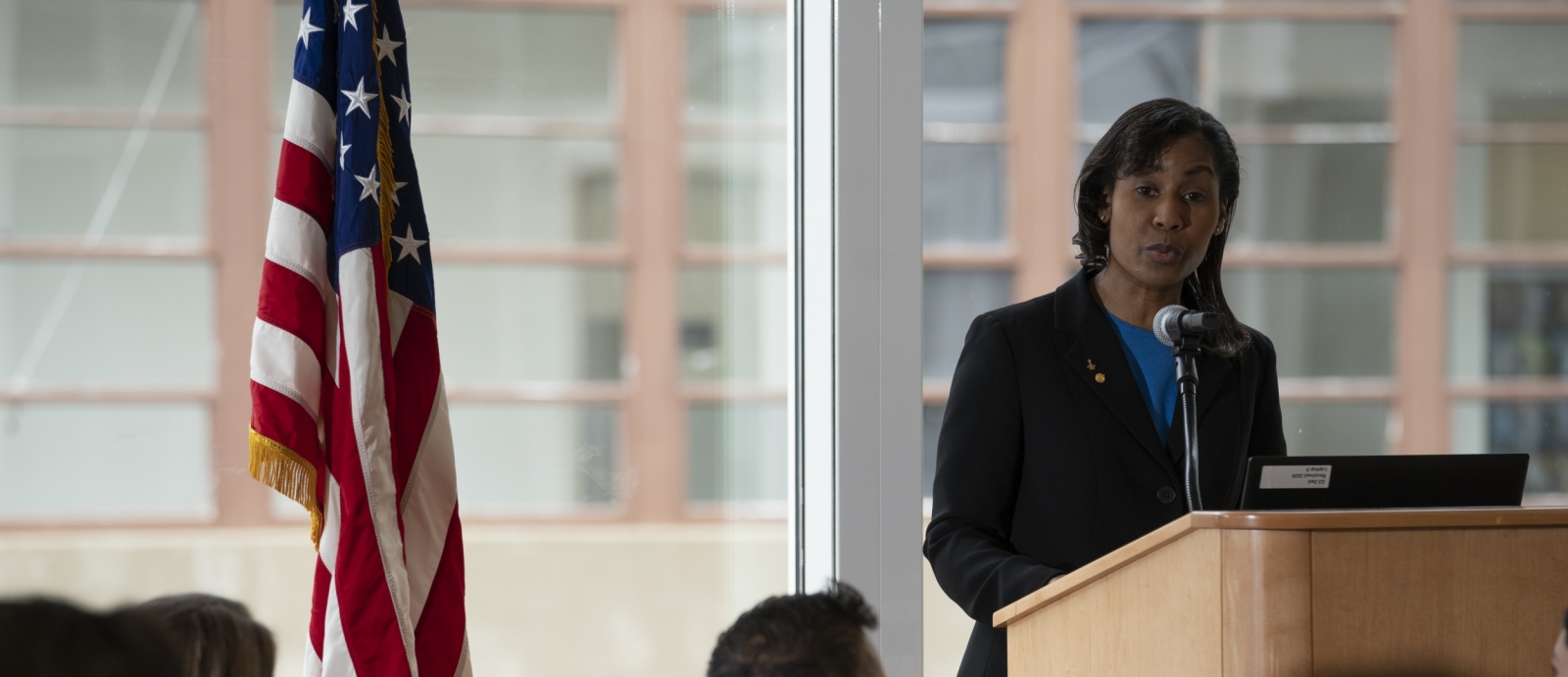 a photo of a woman standing and speaking at a podium next to an American flag