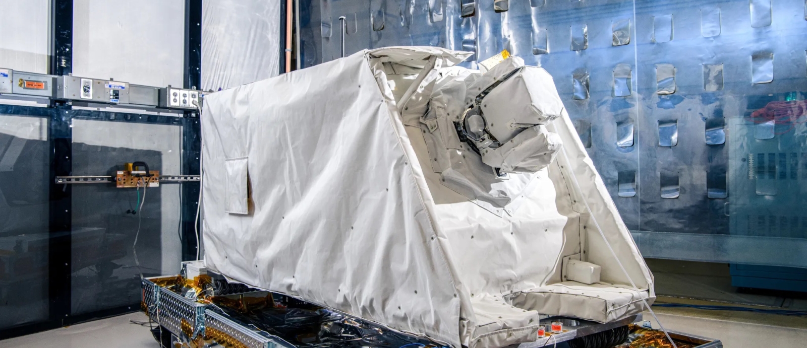 A laser communications terminal approximately the size of a standard refrigerator sits in a cleanroom.