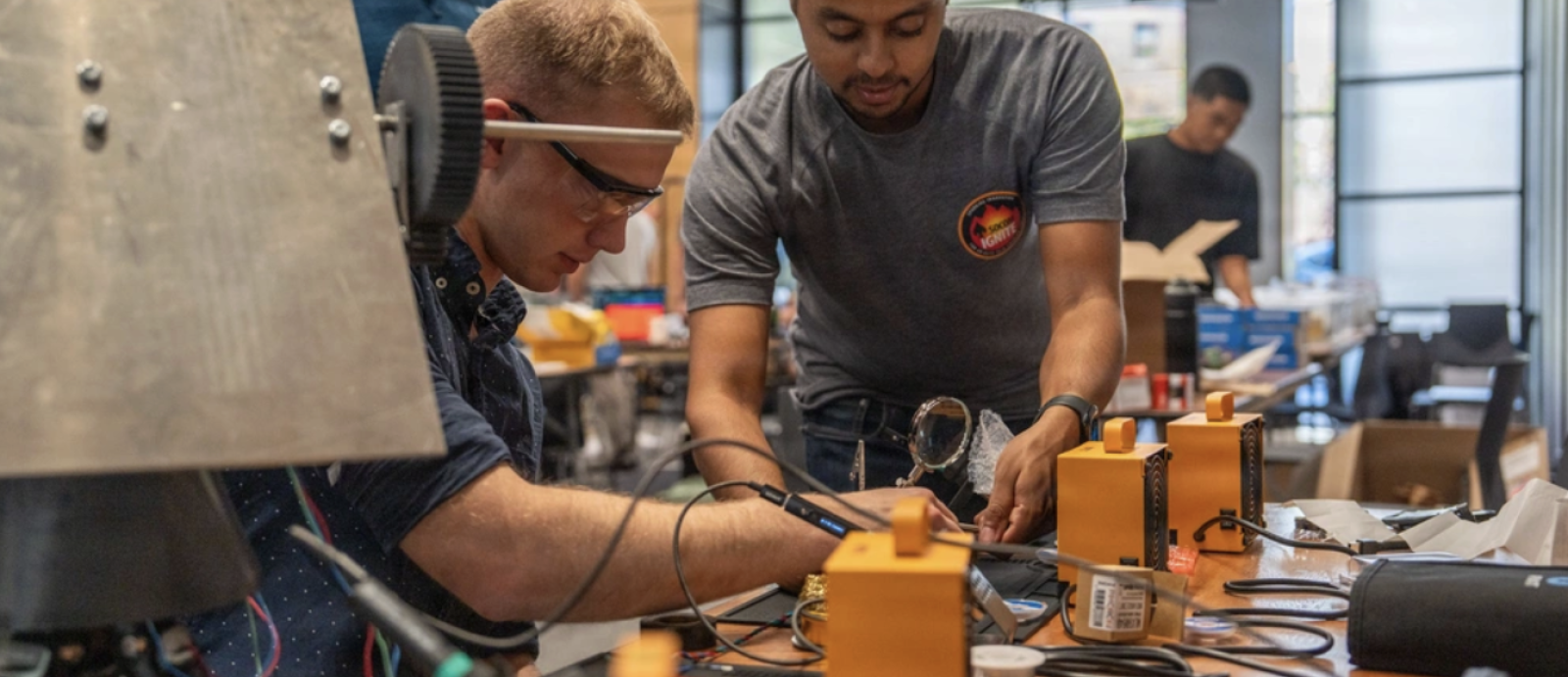 Two SOCOM participants sit at a table full of hardware components. 