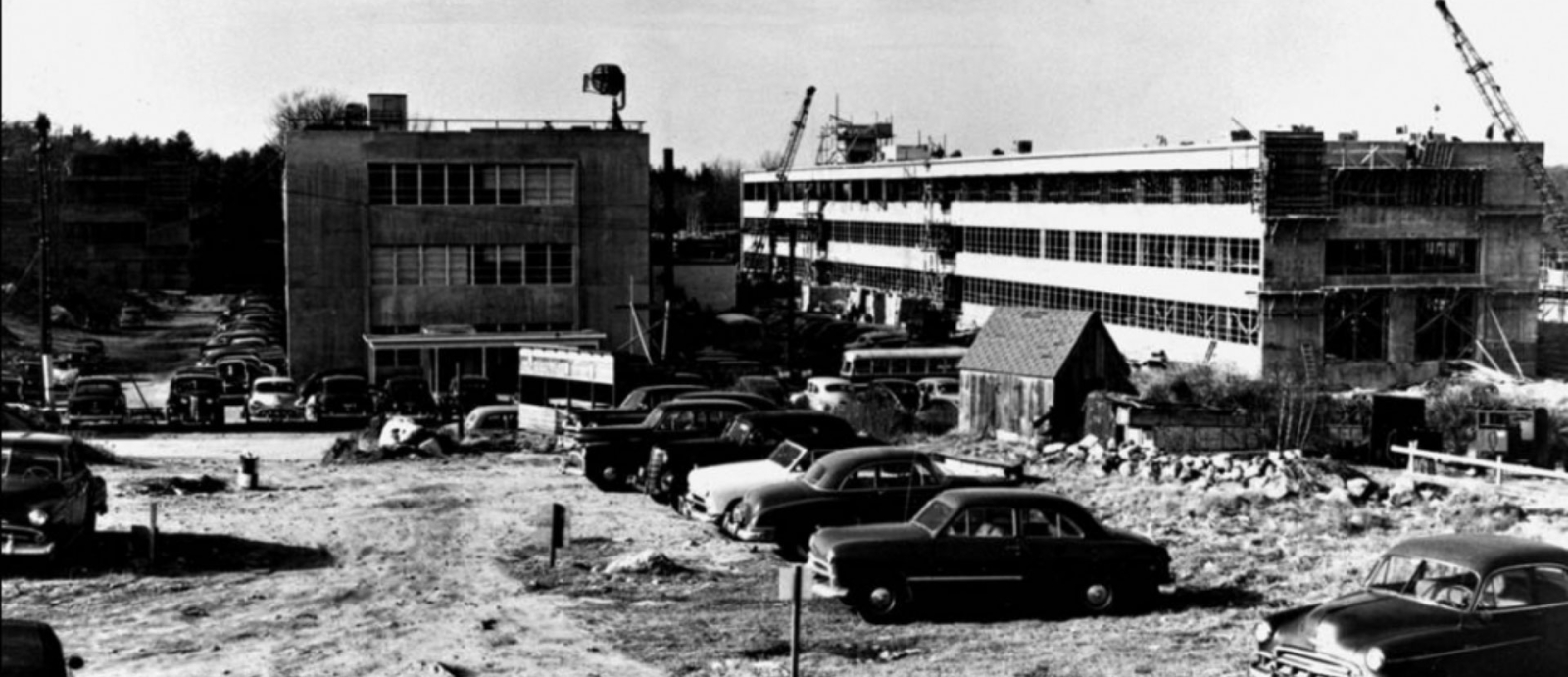 Black and white photo of Lincoln Laboratory under construction with several 1950s era cars.