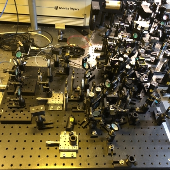 A tabletop showing an optical setup, consisting of dozens of mirrors and other hardware elements.